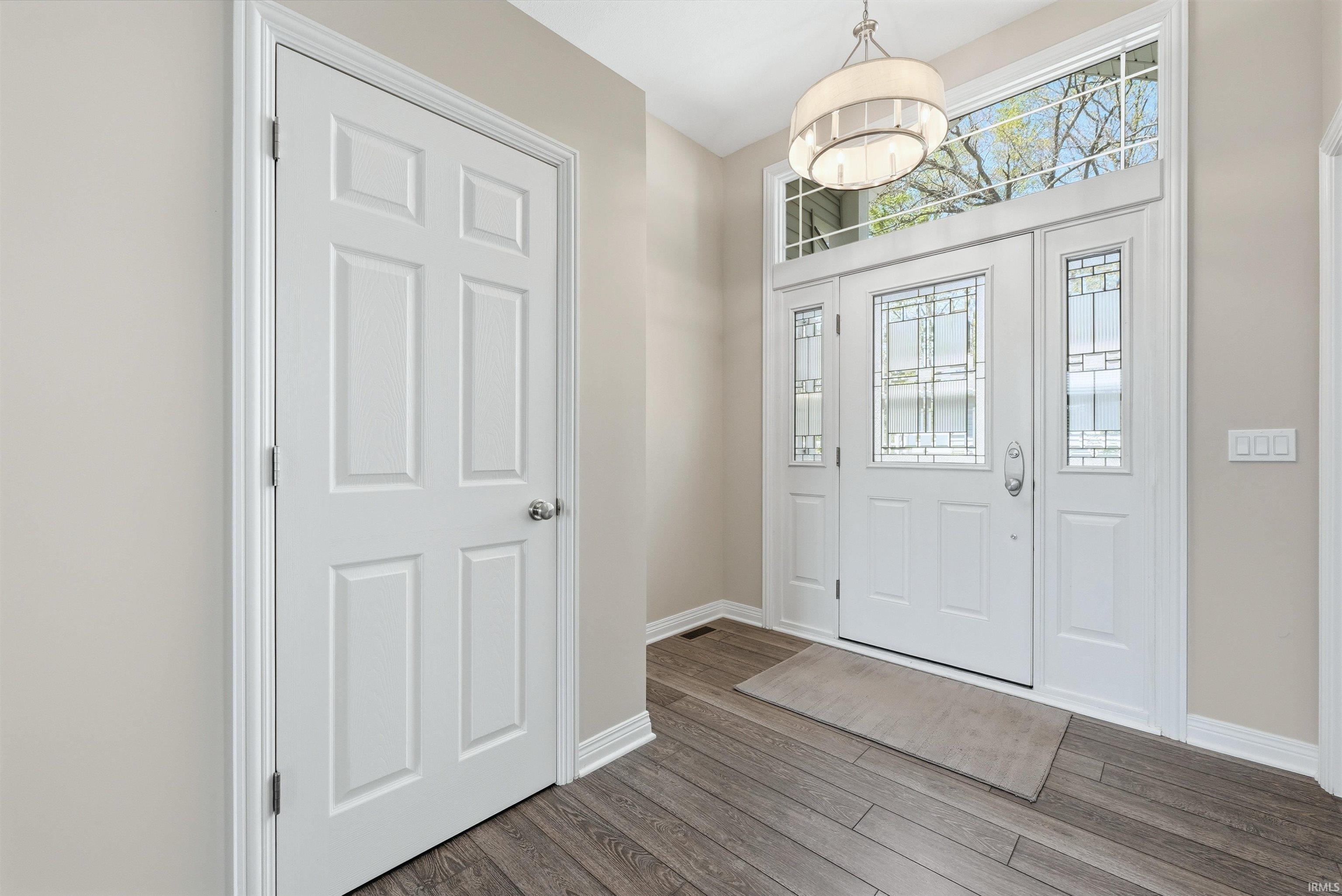 Entryway featuring wood-finish flooring, a six-panel door, and a white front door assembly with leaded glass sidelights and transom windows