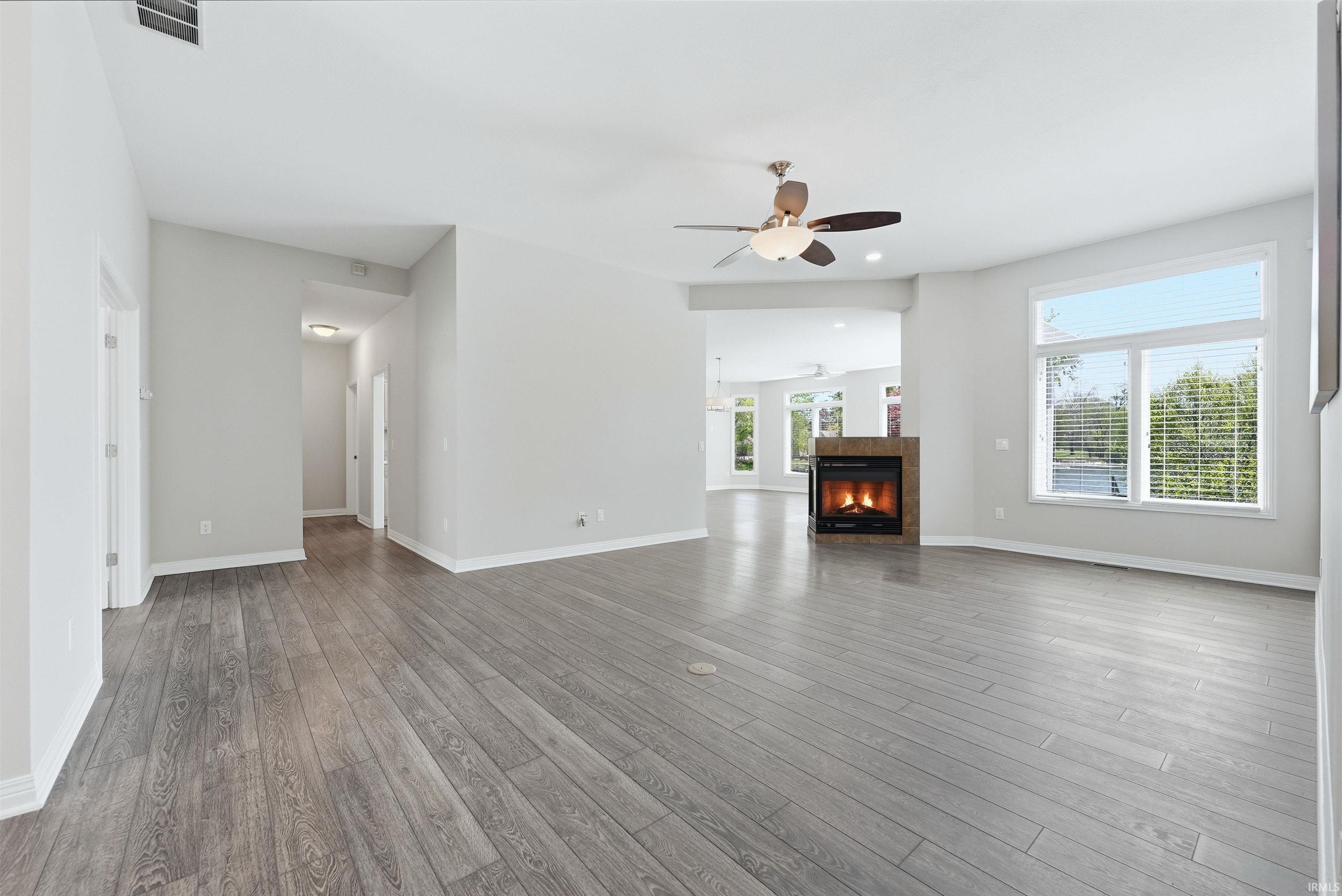 Spacious main living area featuring wide-plank wood-finish flooring, a contemporary fireplace with a stone surround, and multiple large windows with horizontal blinds