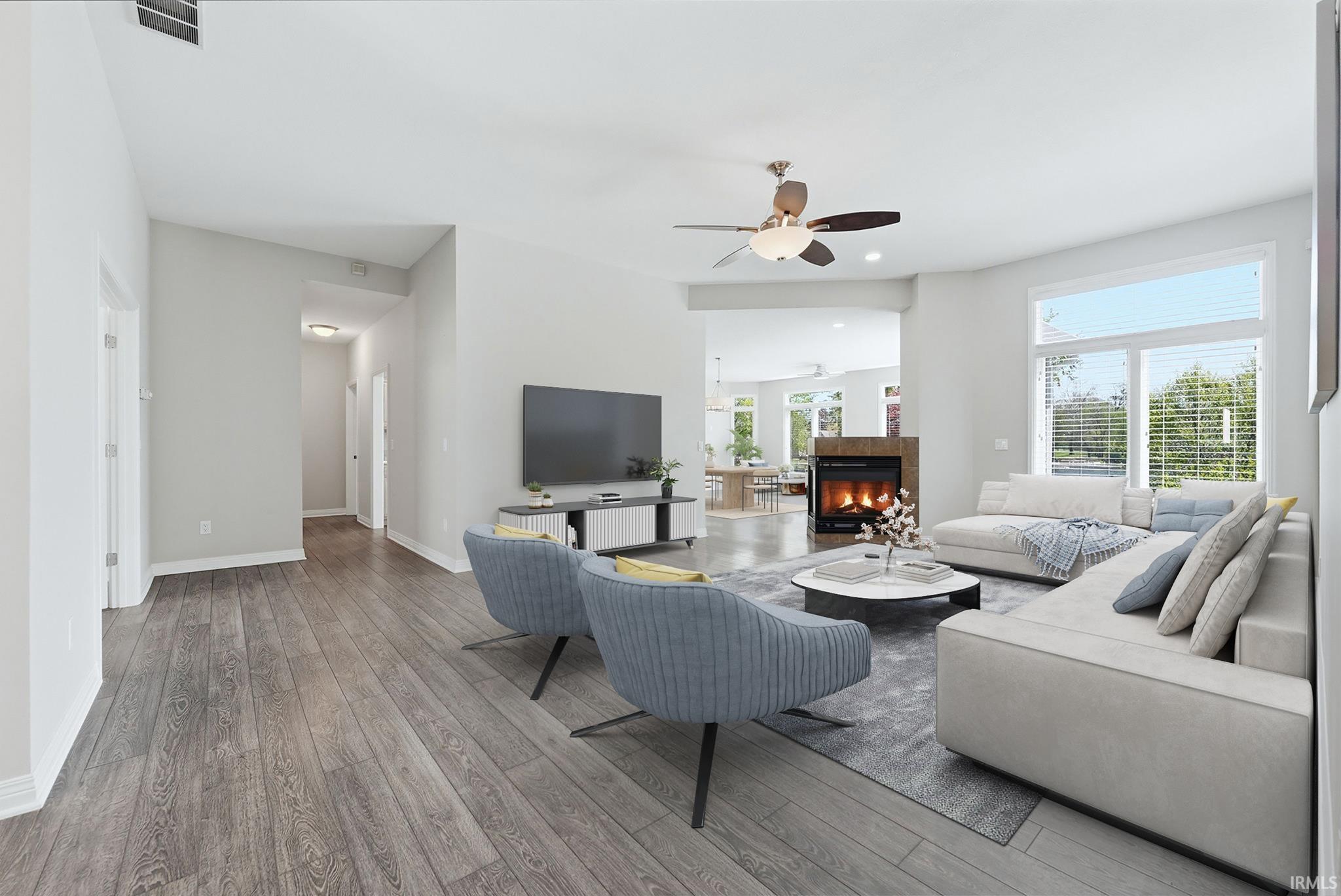 Open-concept living area featuring wood-finish flooring, a contemporary ceiling fan, and a gas fireplace with a stone surround
