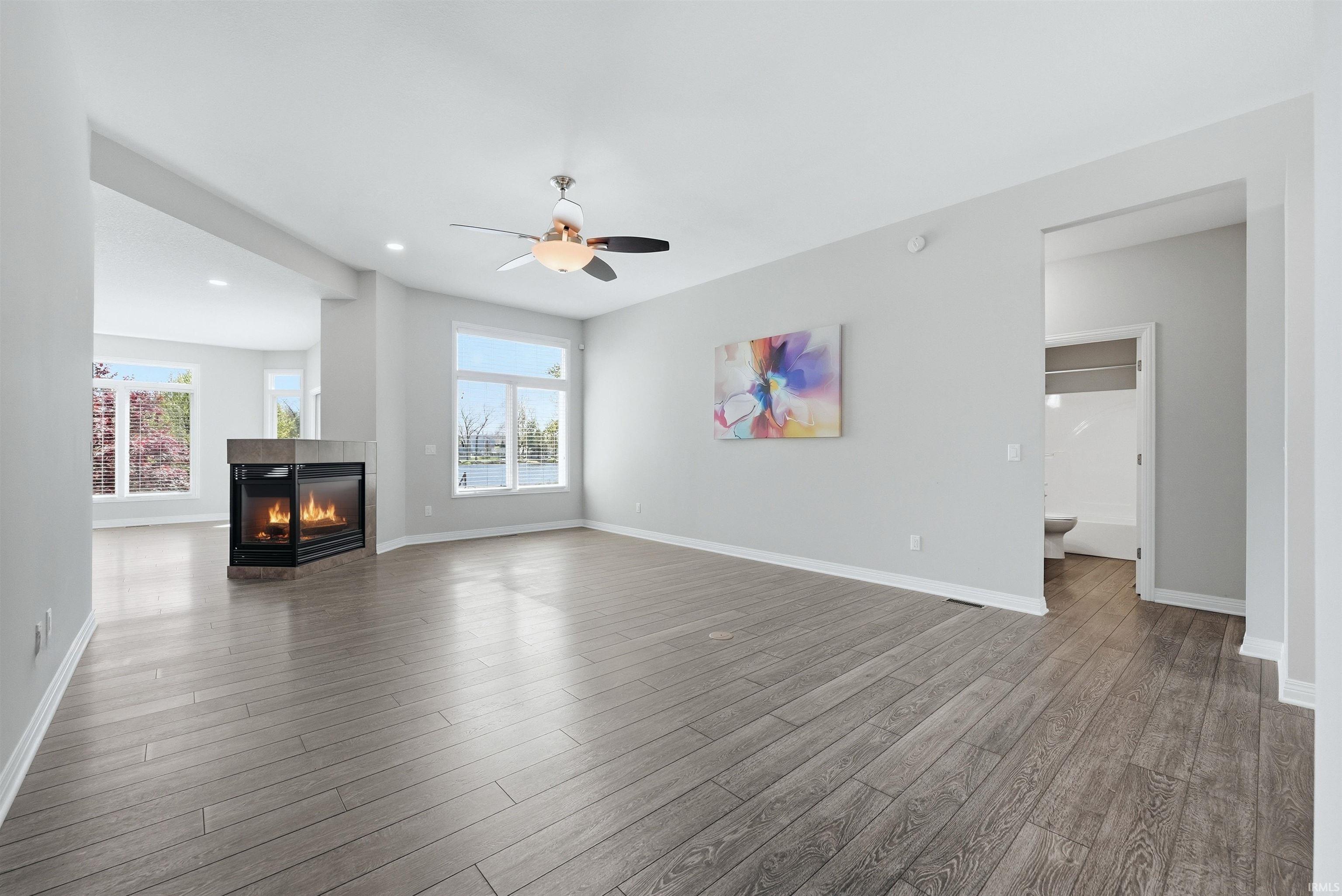 Spacious living area featuring wood-finish flooring, a corner fireplace, and a ceiling fan