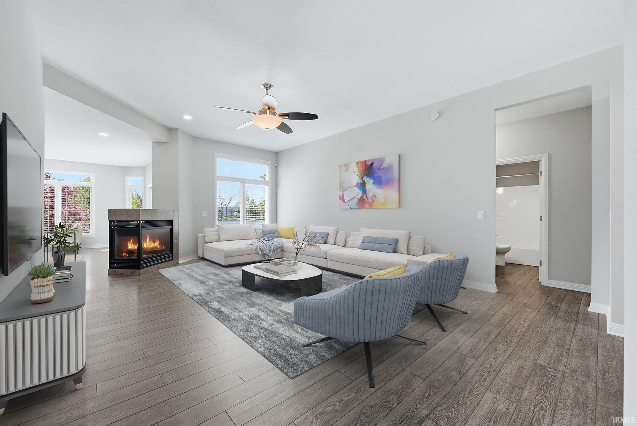 Expansive living area featuring wood-finish flooring, a corner fireplace with stone-look surround, and abundant natural light from multiple windows