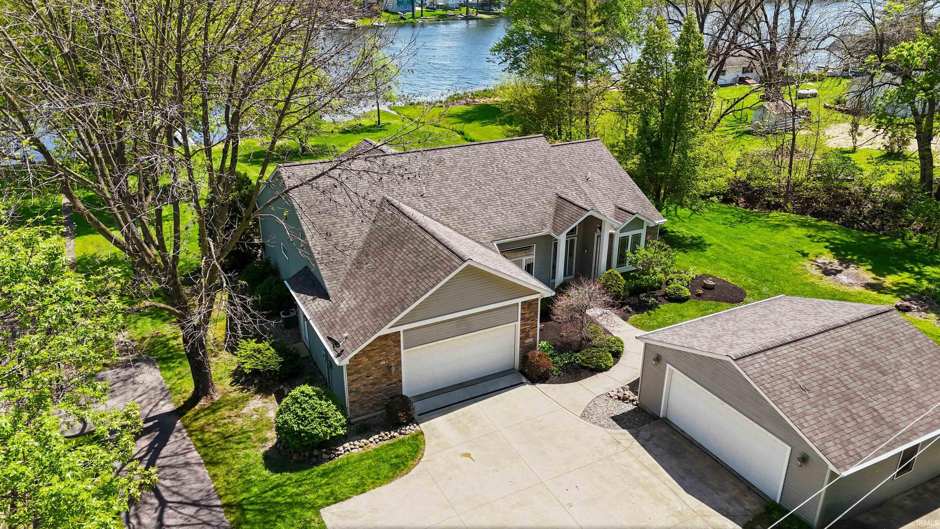Waterfront property featuring a detached garage, expansive lawn, and mature trees