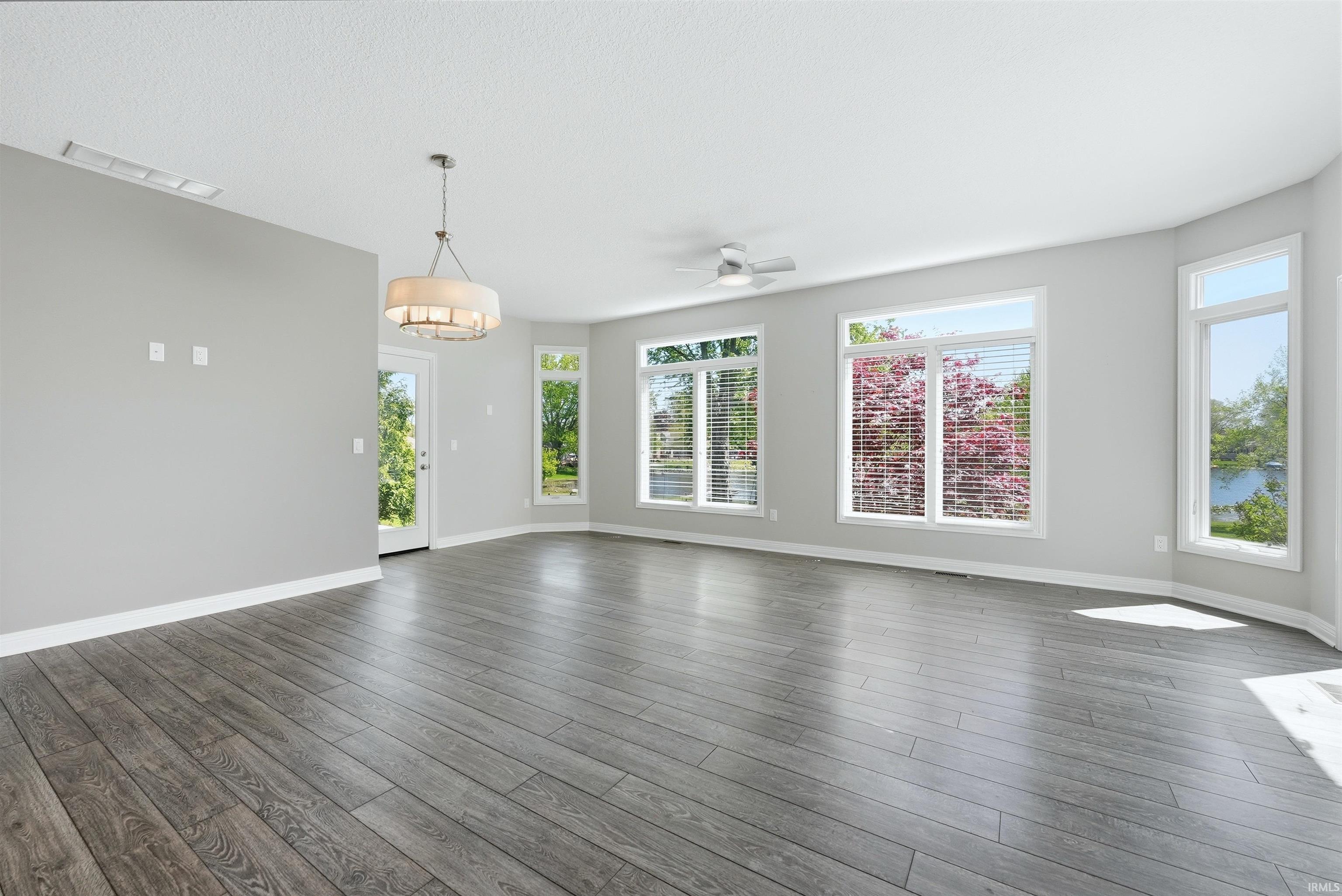Spacious room featuring wood-finish flooring, a contemporary drum pendant light fixture, and multiple large windows with blinds