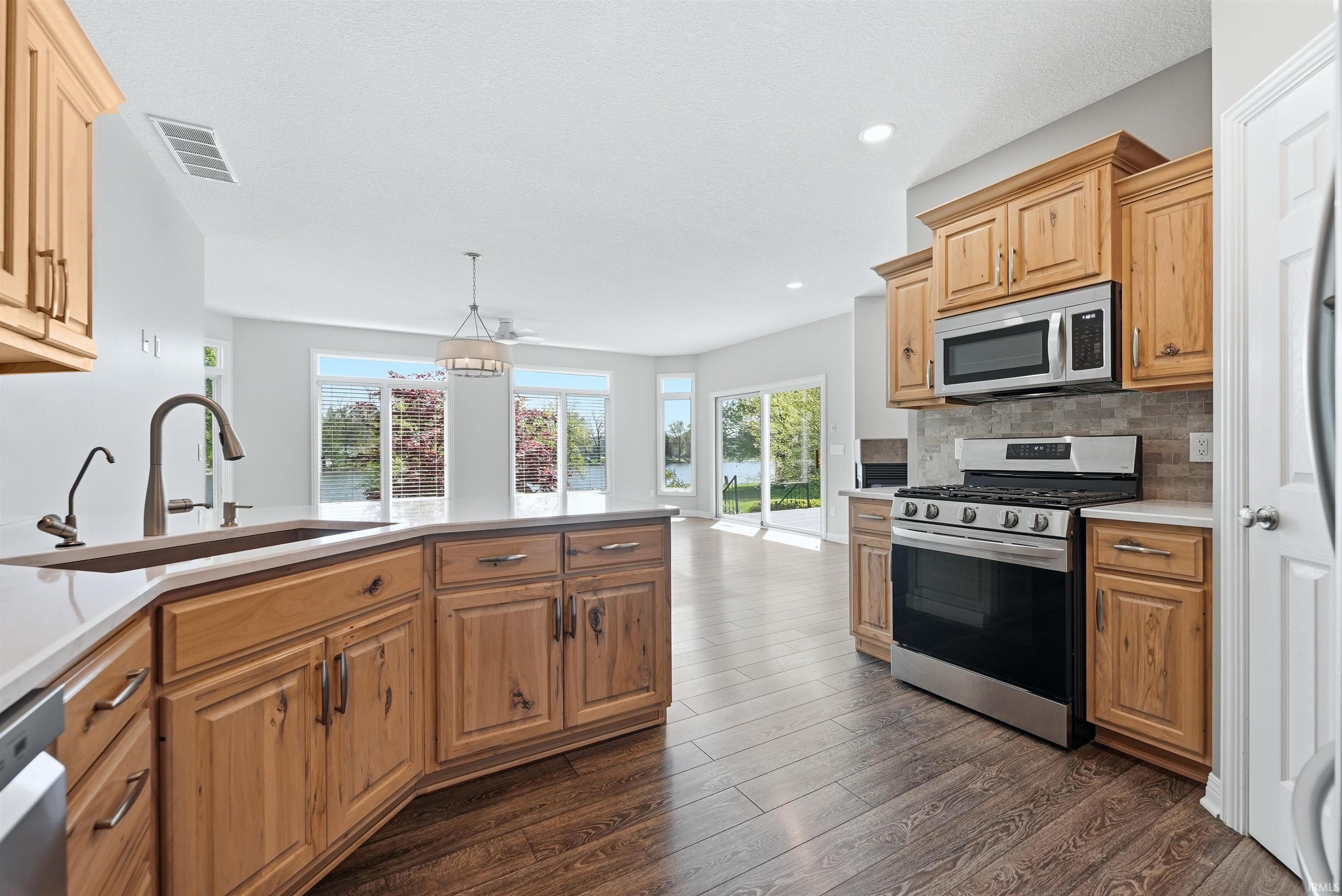 Open-concept kitchen featuring wood cabinetry, stainless steel appliances, light-toned countertops, and wood-finish flooring