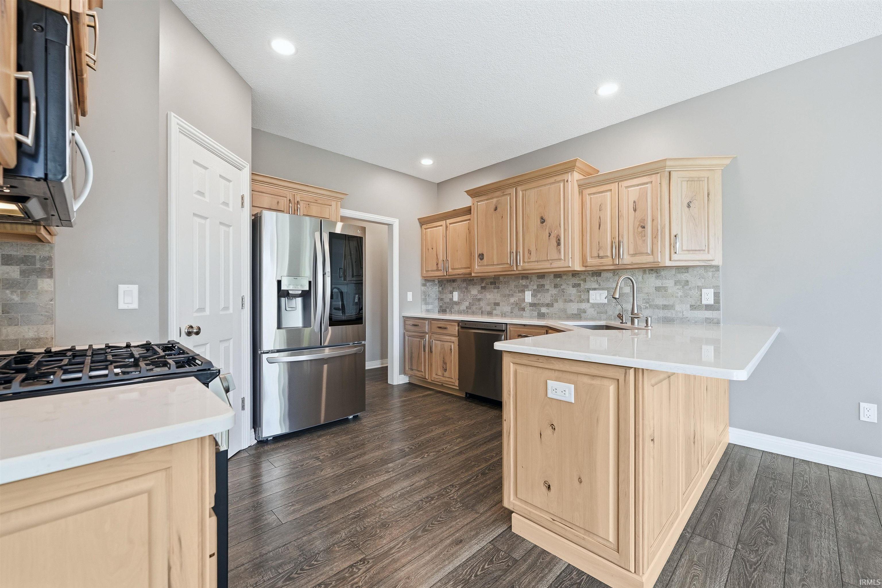 Kitchen featuring wood-finish cabinetry, stainless steel appliances, a tile backsplash, and light-toned countertops