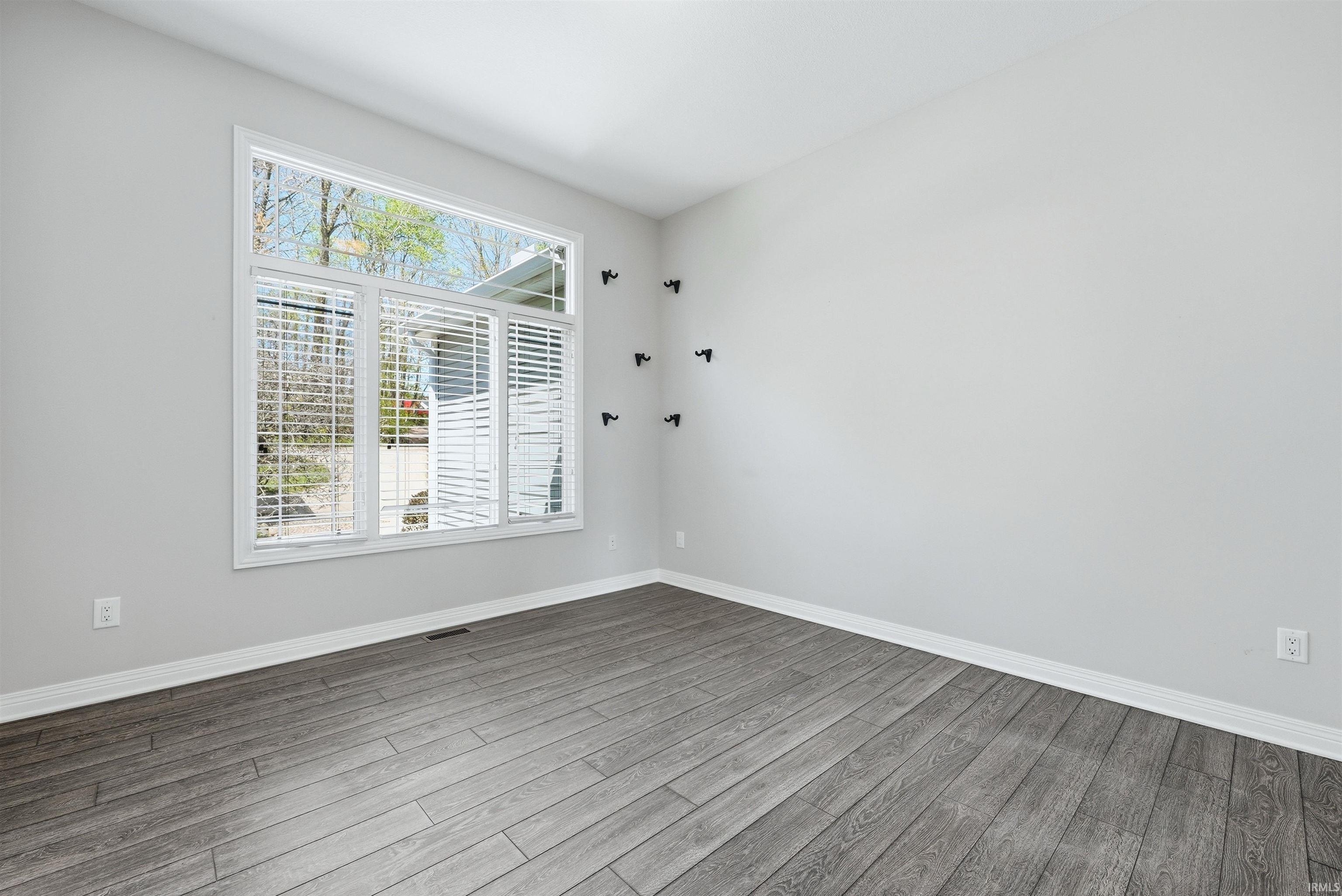 Room featuring a large white-framed window with integrated blinds, wood-finish flooring, light grey painted walls, and white trim