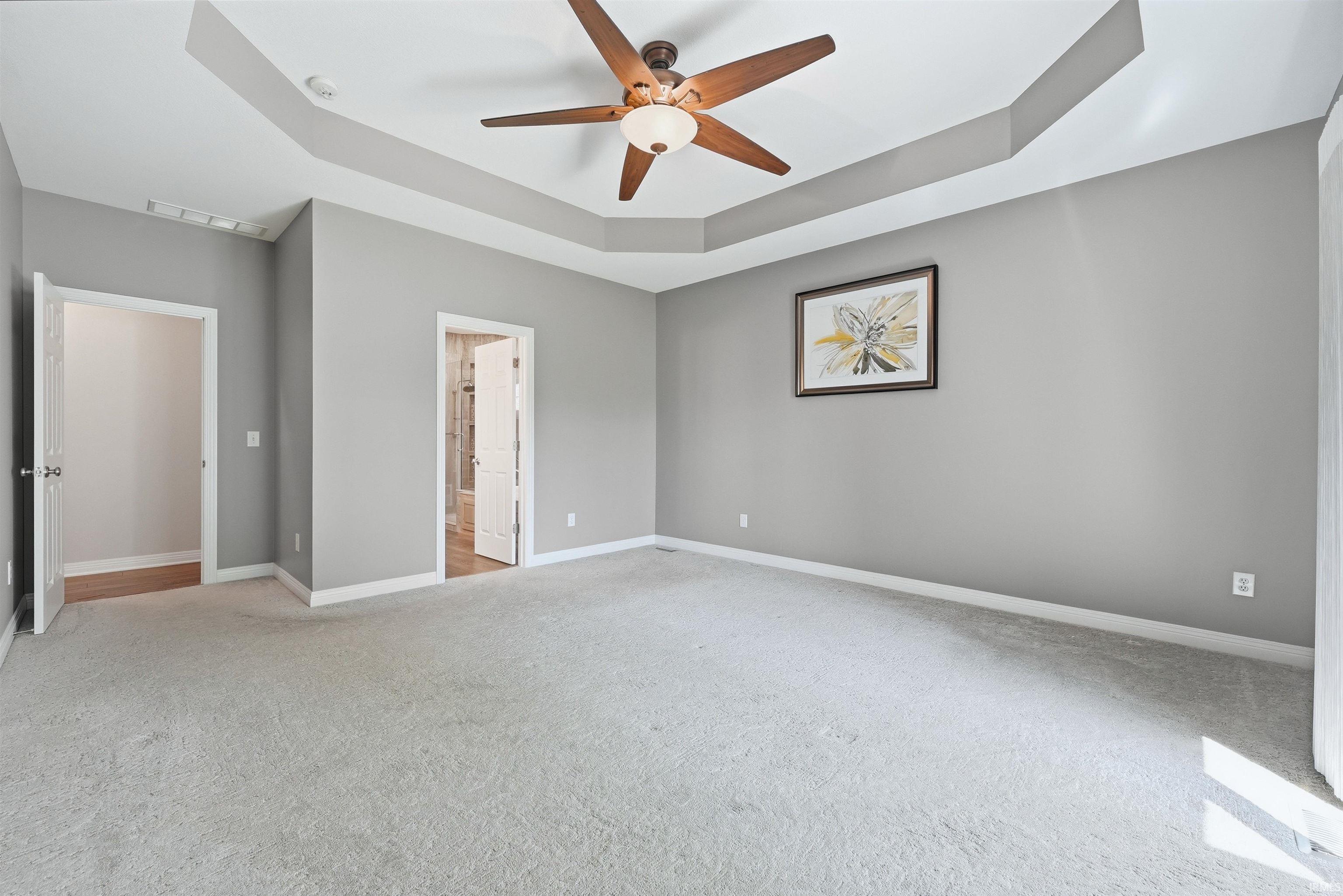 Expansive room featuring a tray ceiling, ceiling fan with integrated lighting, two panel doors, and neutral carpeting