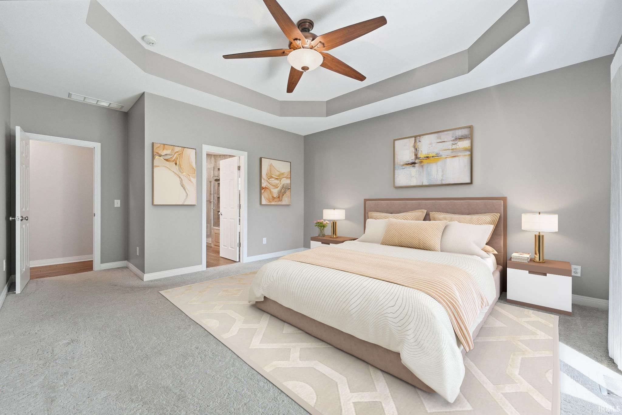 Spacious bedroom featuring light gray walls, a tray ceiling, and a ceiling fan with integrated lighting