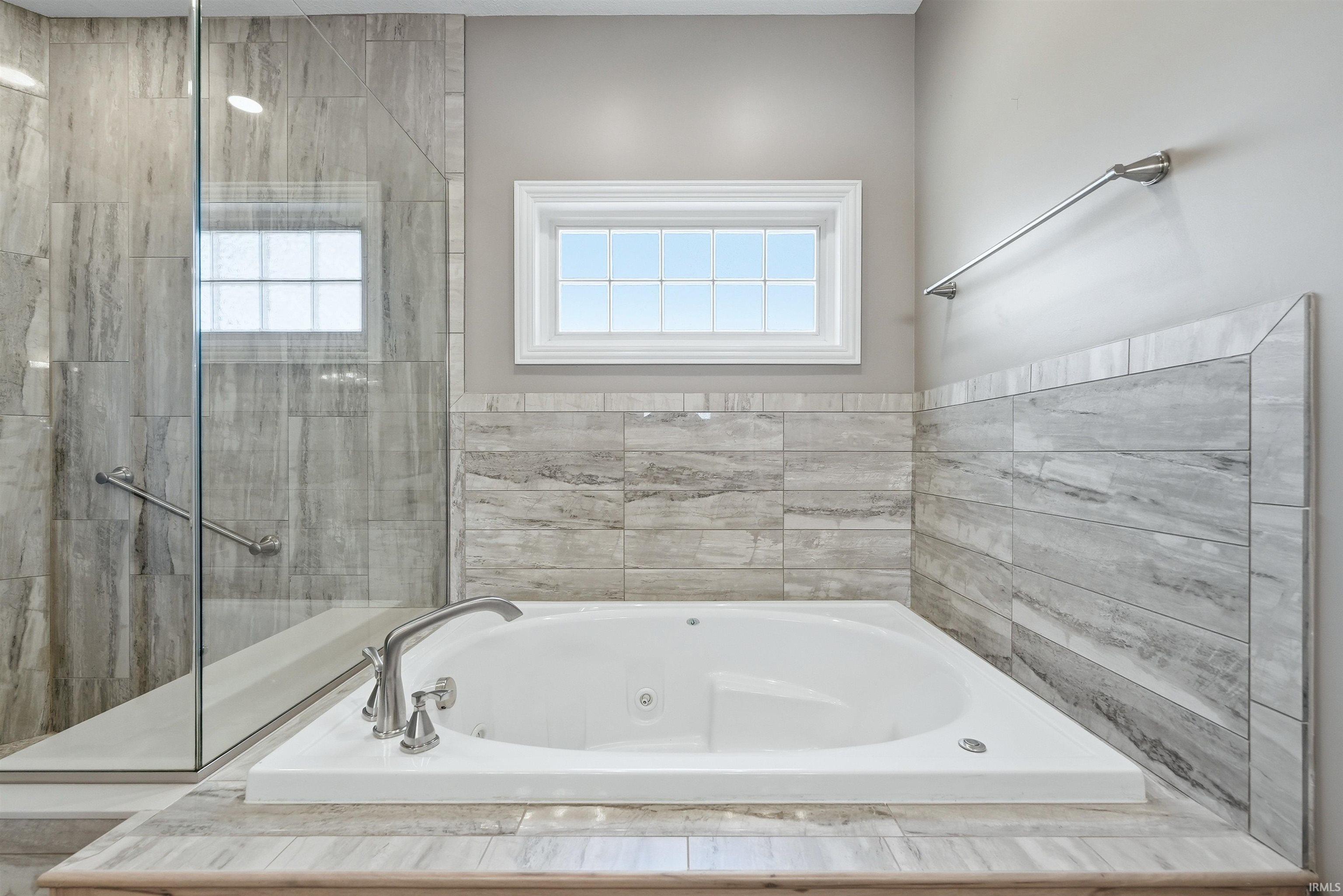 Soaking tub with brushed nickel fixtures, surrounded by a light-toned wood-finish tile wainscoting