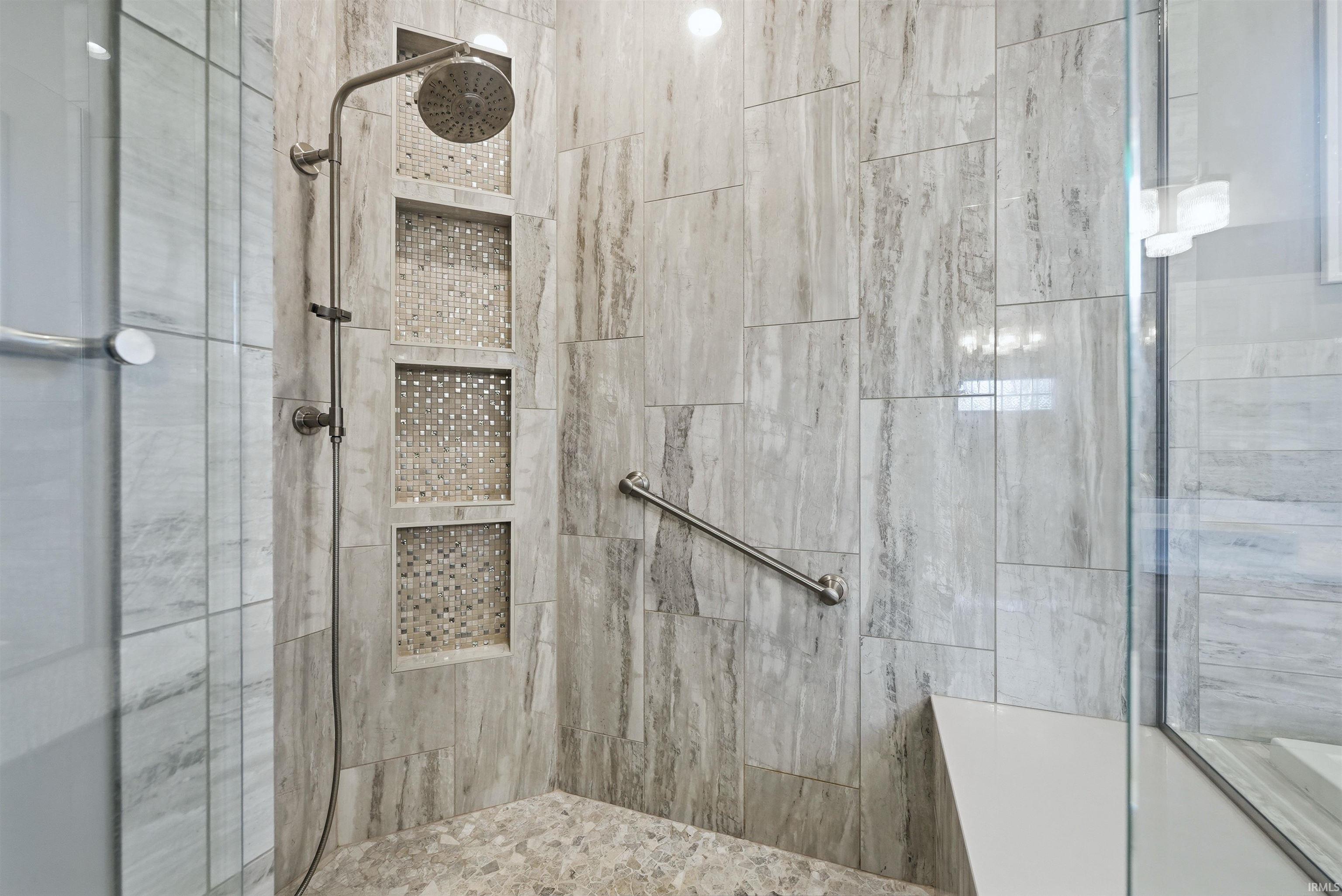Walk-in shower featuring large format stone-look tile, three recessed mosaic-tiled niches, a rainfall showerhead, and a built-in bench