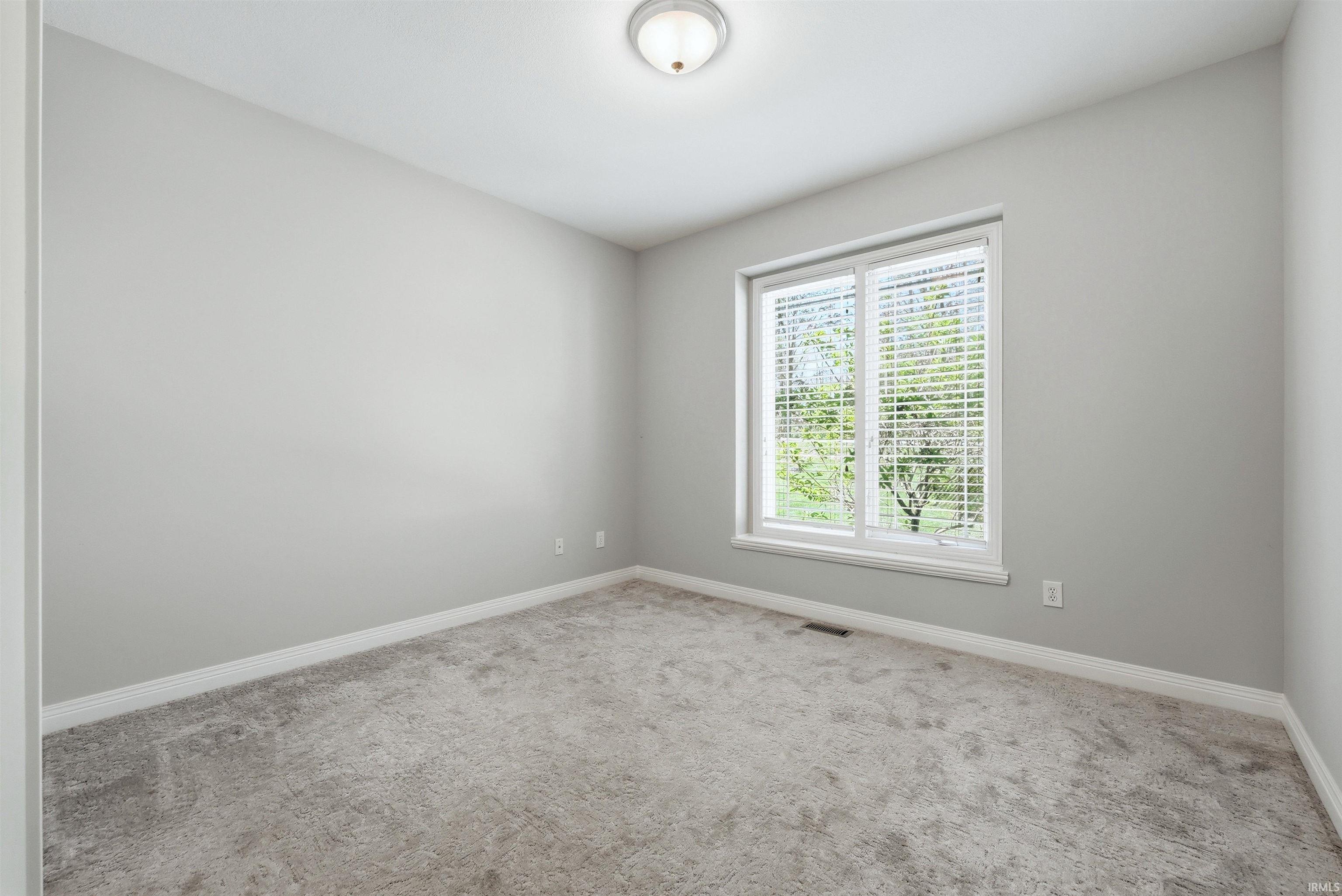 Bright interior room featuring a neutral color palette, grey carpeting, white baseboards, and a window with white blinds