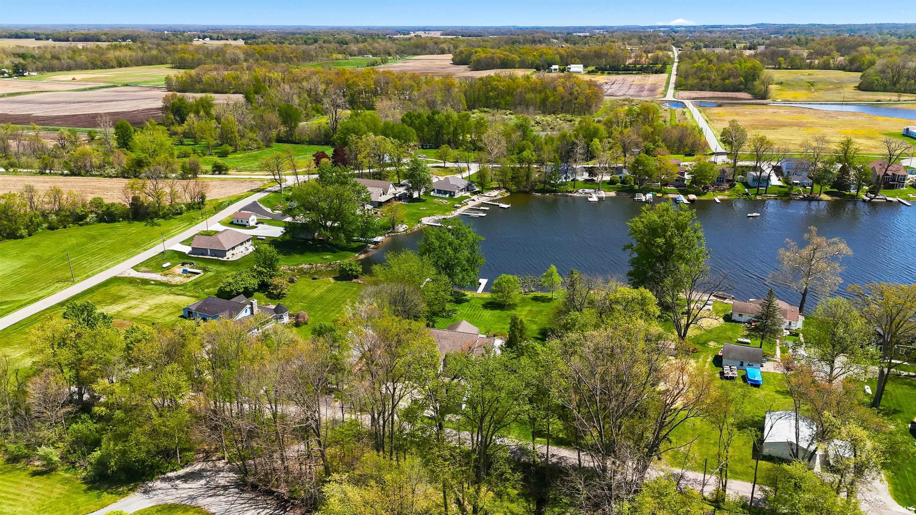 Expansive aerial view showcasing properties bordering a substantial body of water, surrounded by agricultural fields and woodland areas