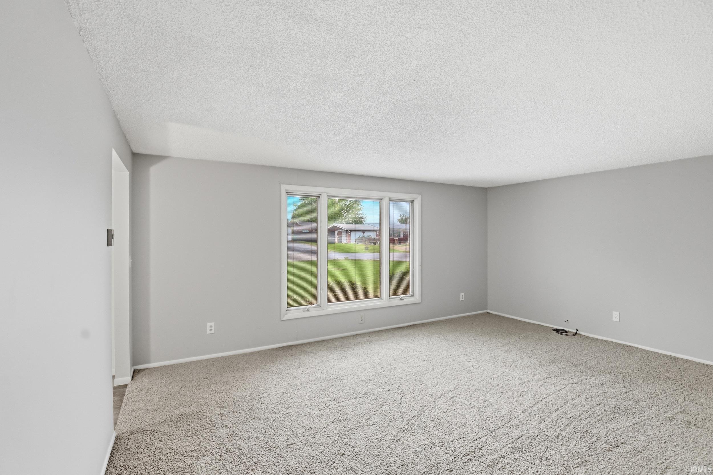 Spacious room featuring light gray walls, textured ceiling, and a large multi-pane window