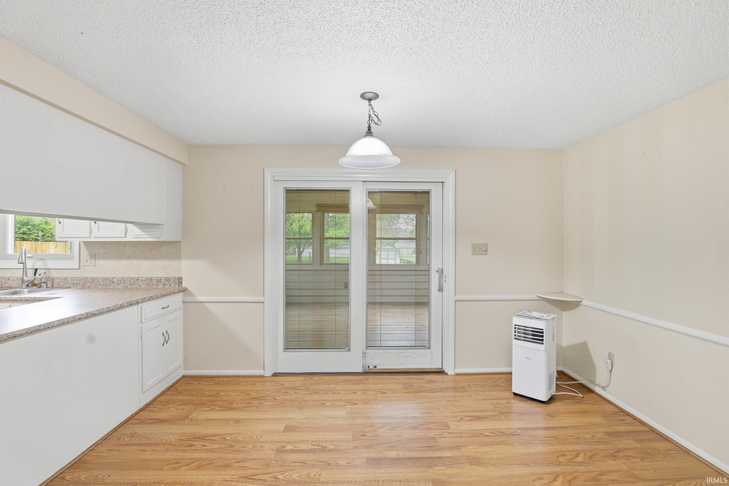 Kitchen and dining area featuring wood-finish flooring, white cabinetry, speckled countertops, and a white sink with a chrome faucet