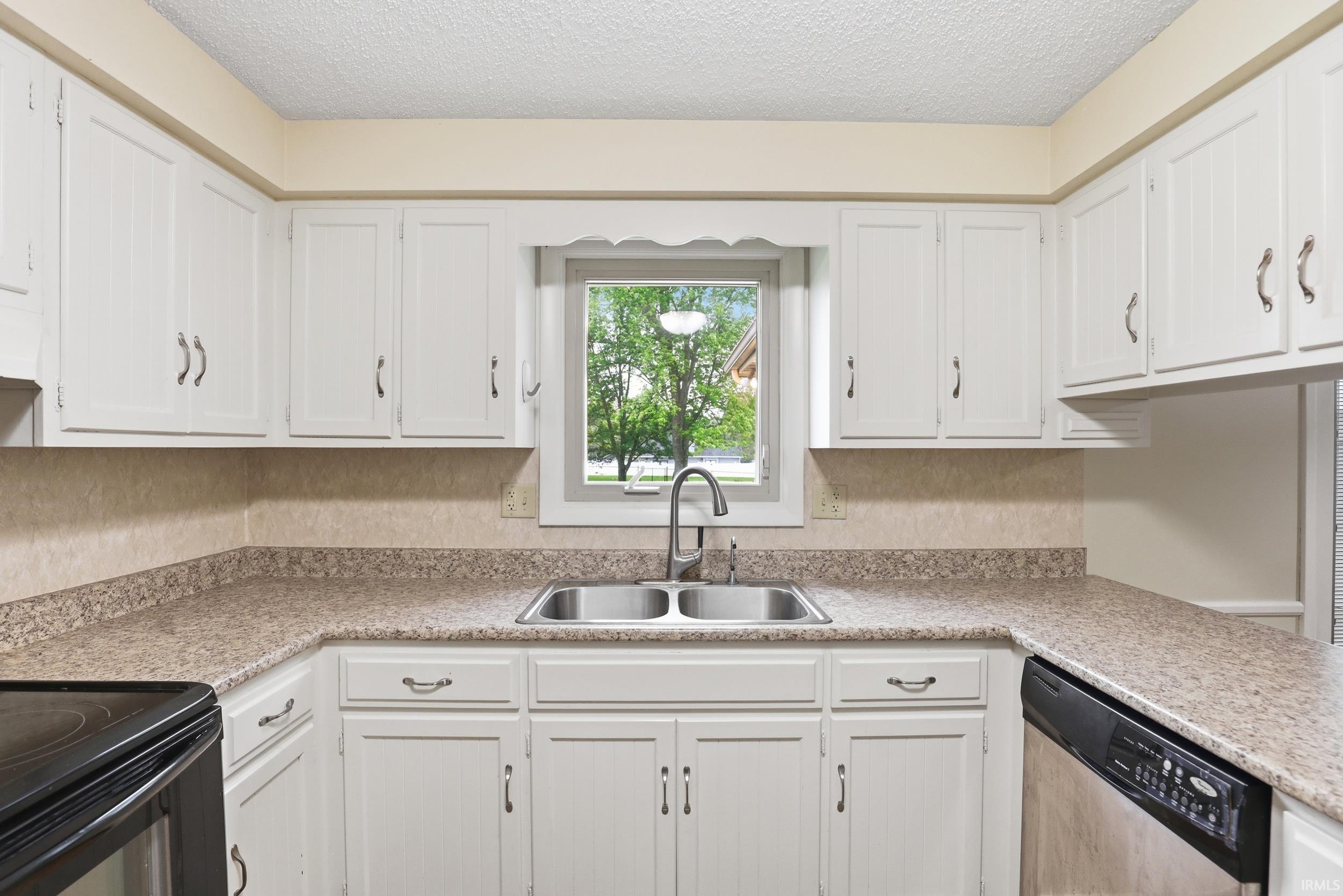 Kitchen featuring white cabinetry with silver-tone hardware, a double basin stainless steel sink, and speckled countertops