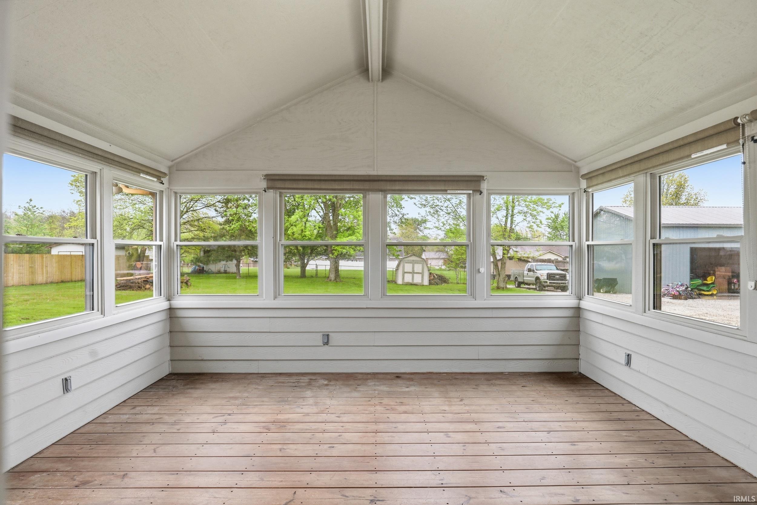 Sunroom featuring expansive multi-pane windows, wood-finish flooring, white horizontal paneling, and a vaulted ceiling