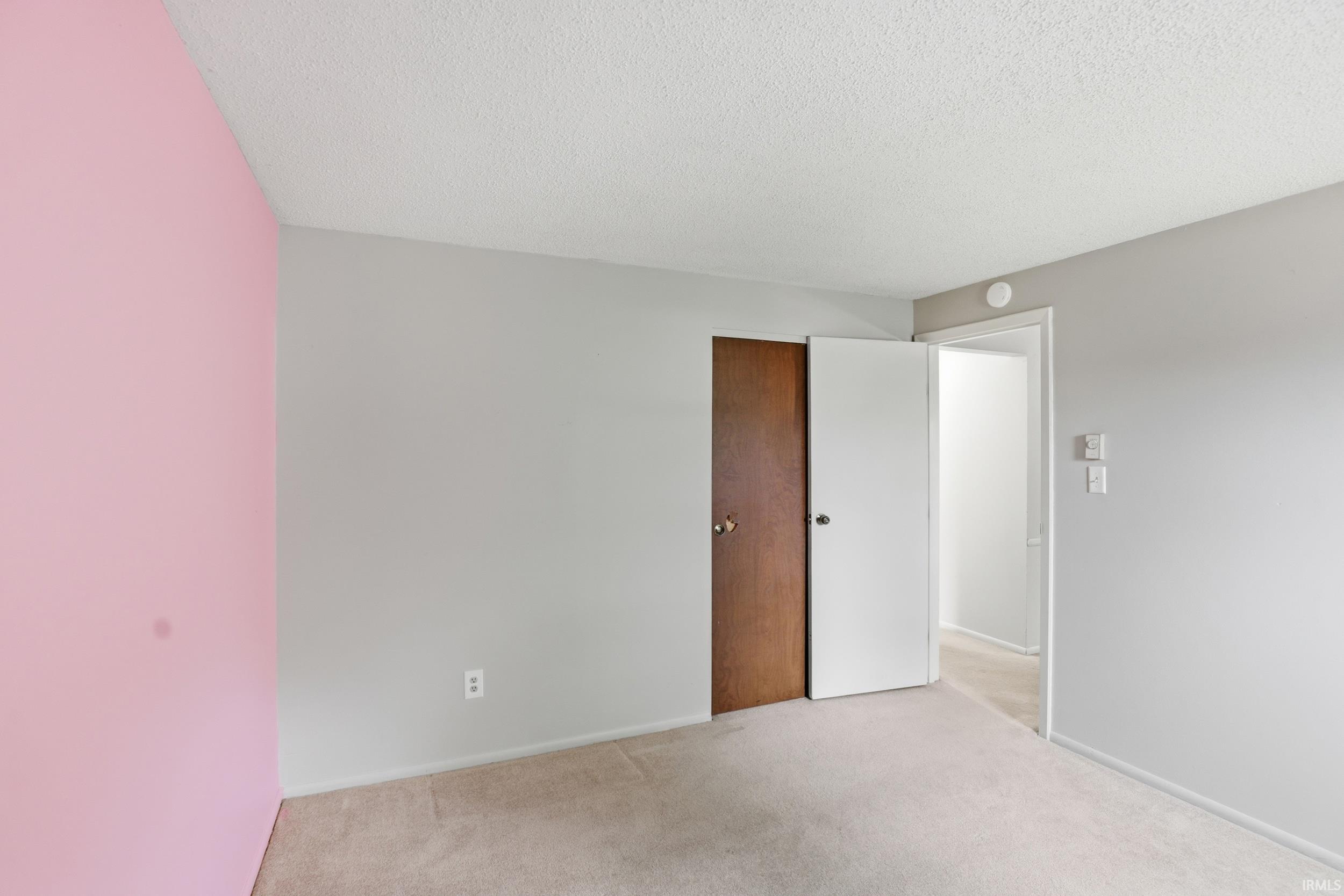 Carpeted room with a textured ceiling, featuring a partial pink accent wall