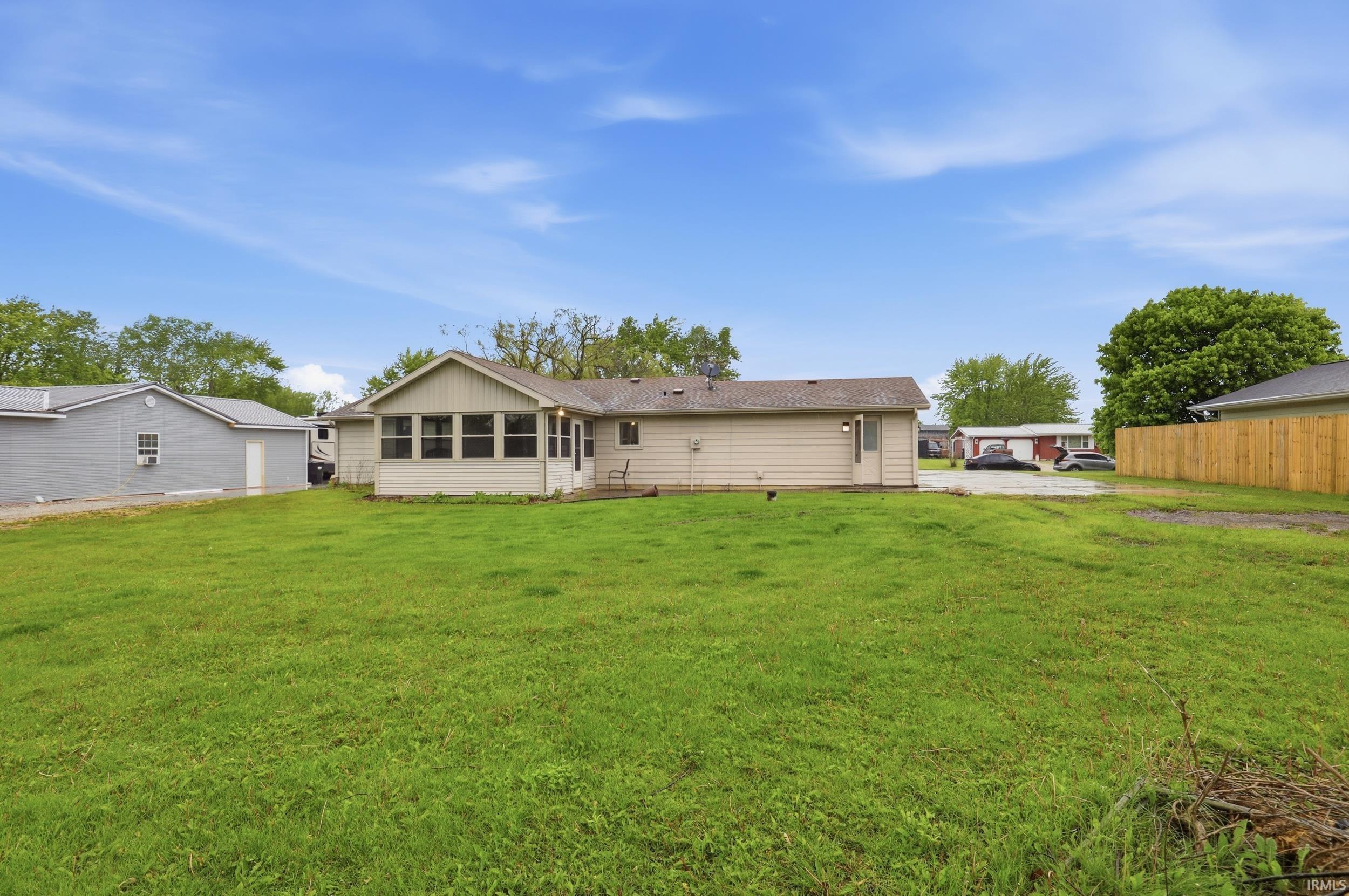 Expansive green space featuring a single-story residence with a sunroom, a detached auxiliary structure, and a perimeter fence