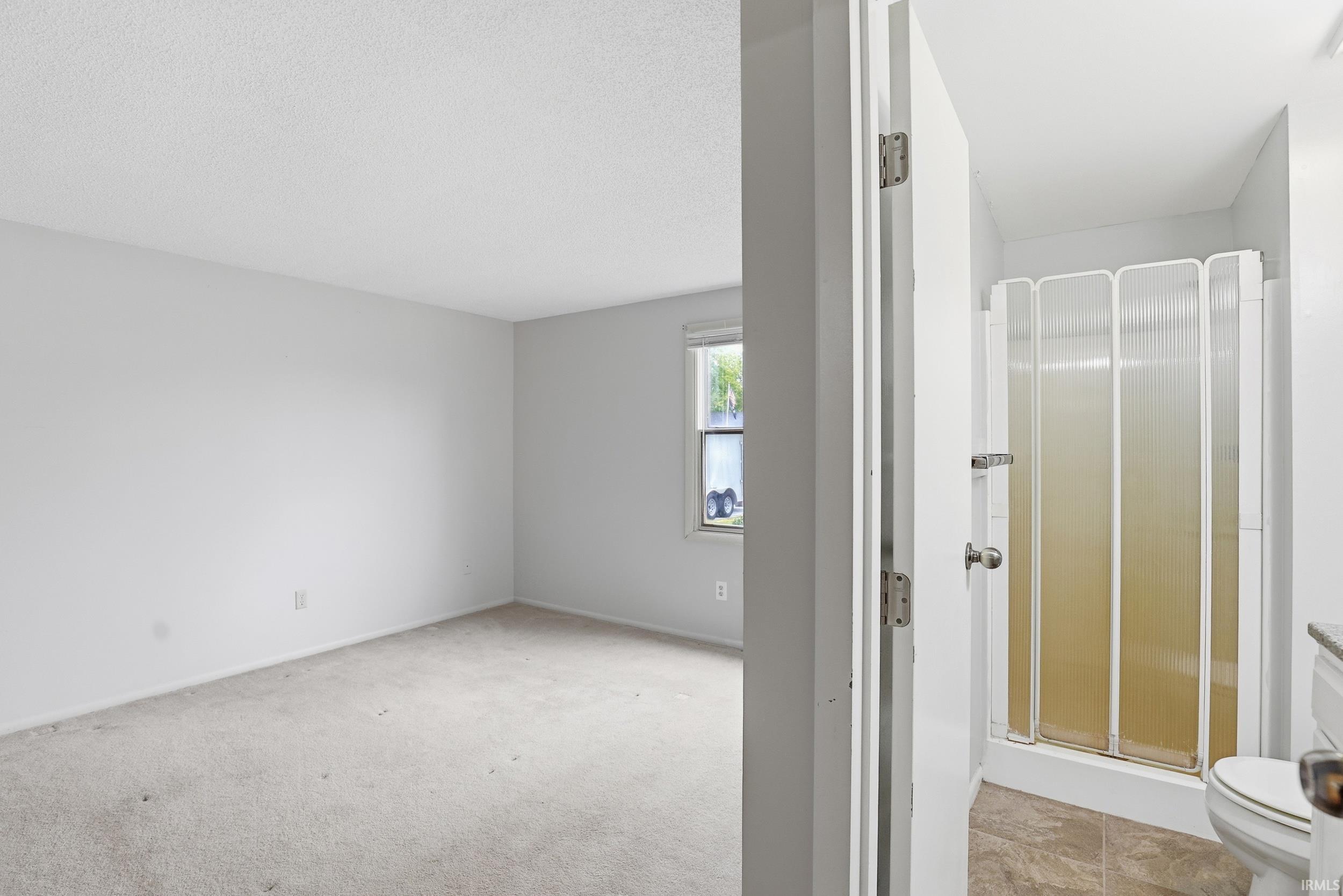 Carpeted room with a single window and textured white walls
