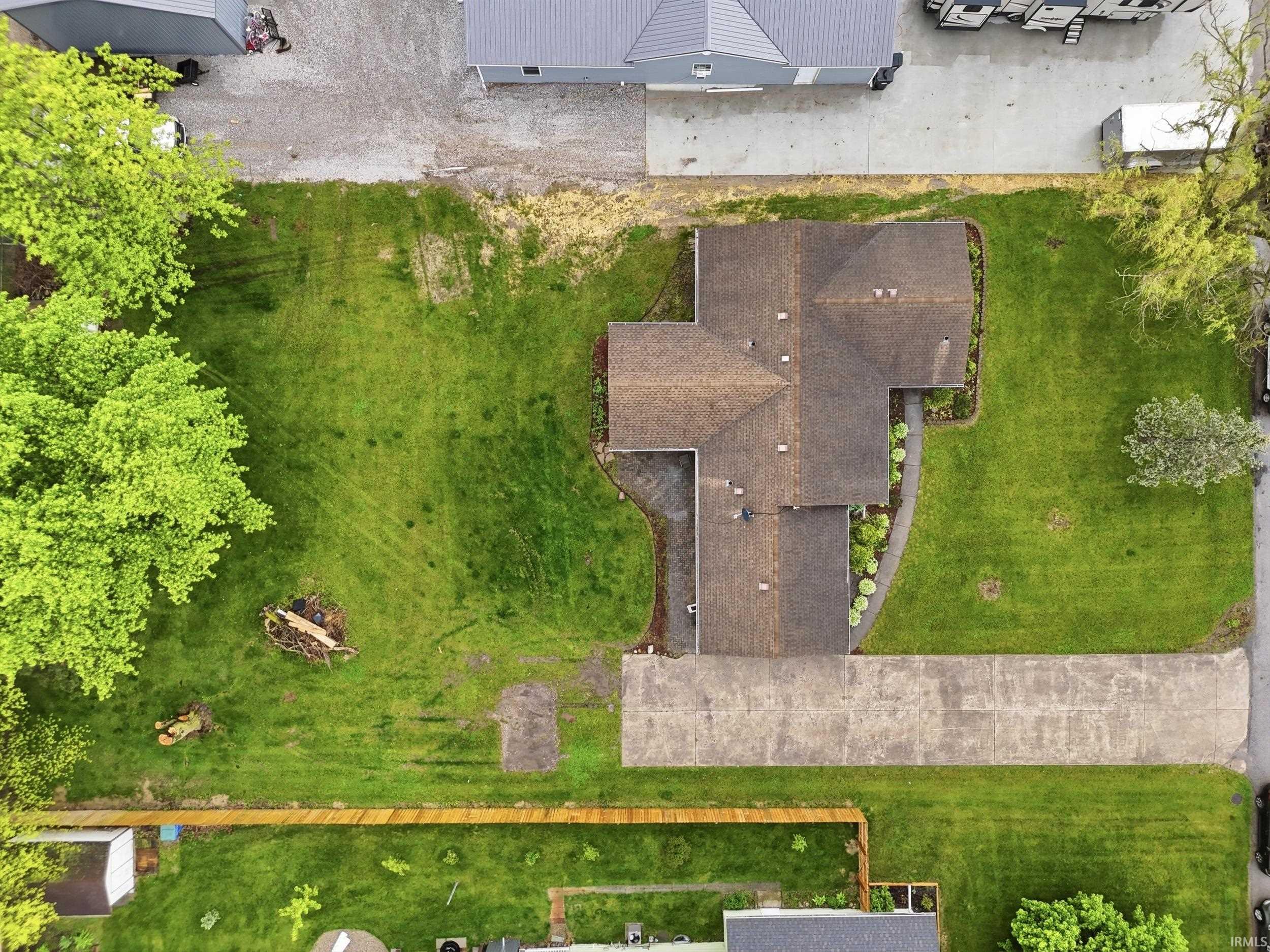 Single-story residence with a brown shingle roof, expansive green lawn, mature trees, and concrete driveway