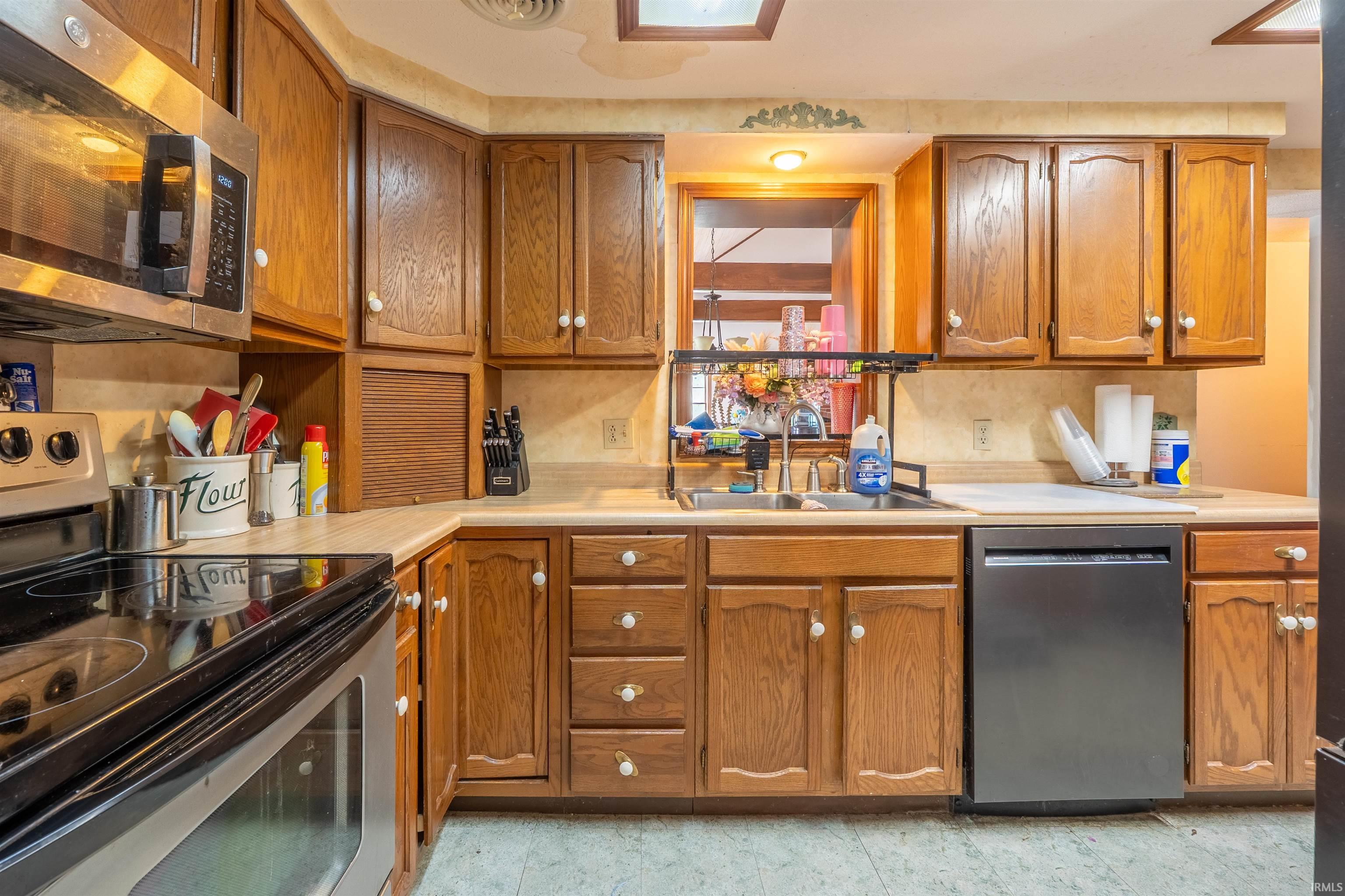 Kitchen featuring wood cabinetry, stainless steel microwave, black electric range, stainless steel sink, and black dishwasher