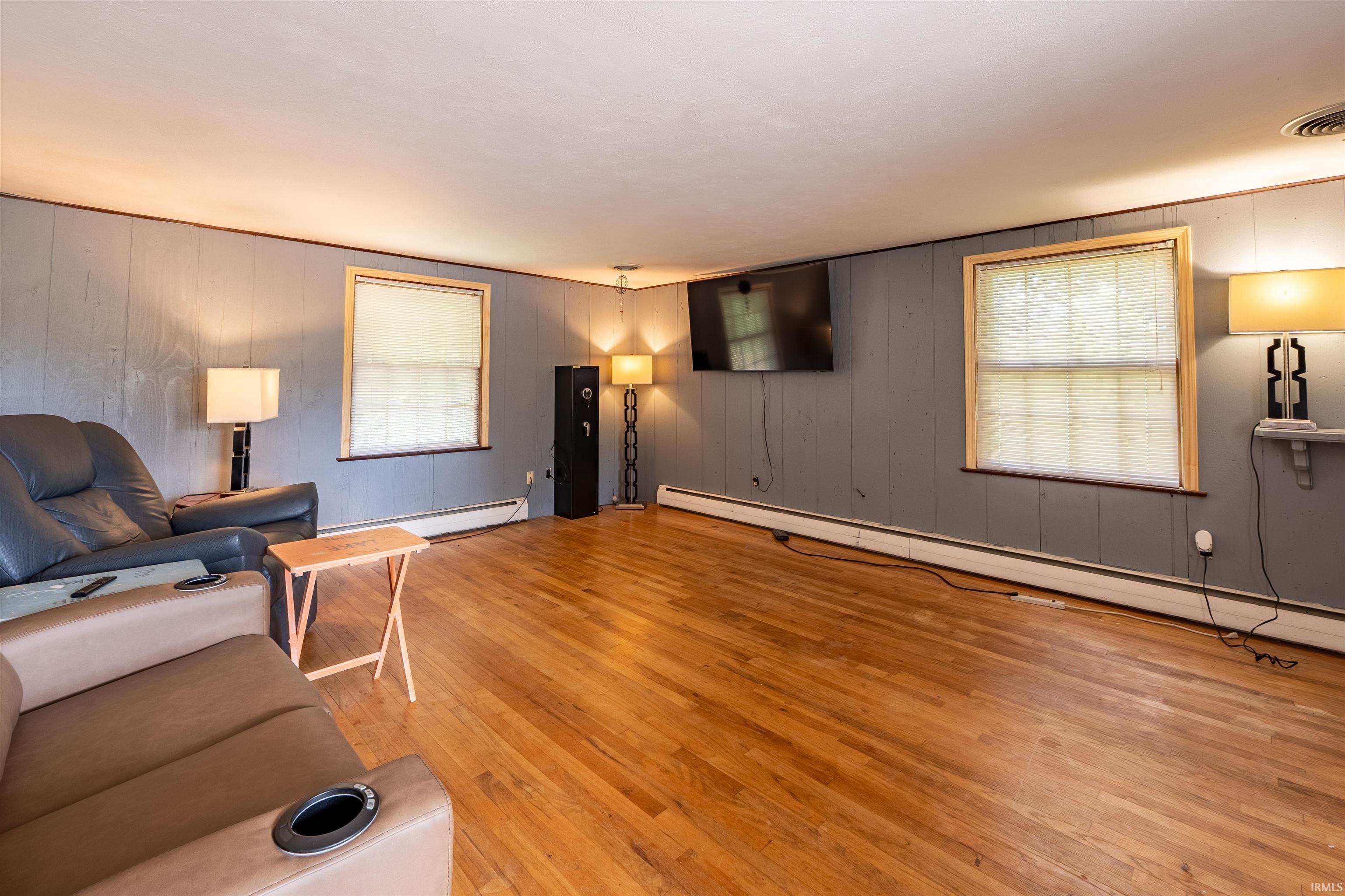 Spacious interior room featuring wood-finish flooring, two windows with wooden trim, and textured wall paneling