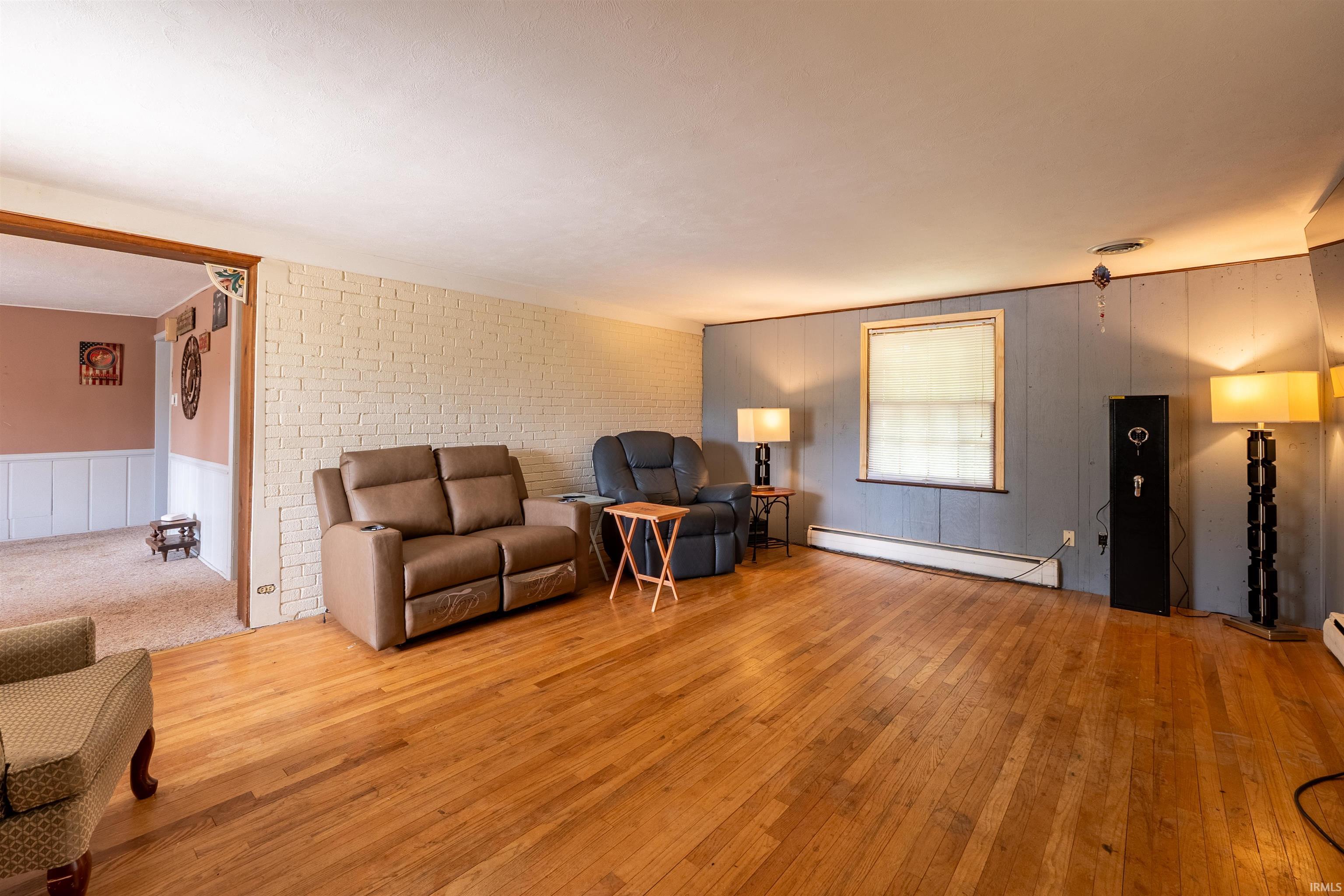 Hardwood flooring extends across this room, featuring a white painted brick accent wall and a paneled wall with a window