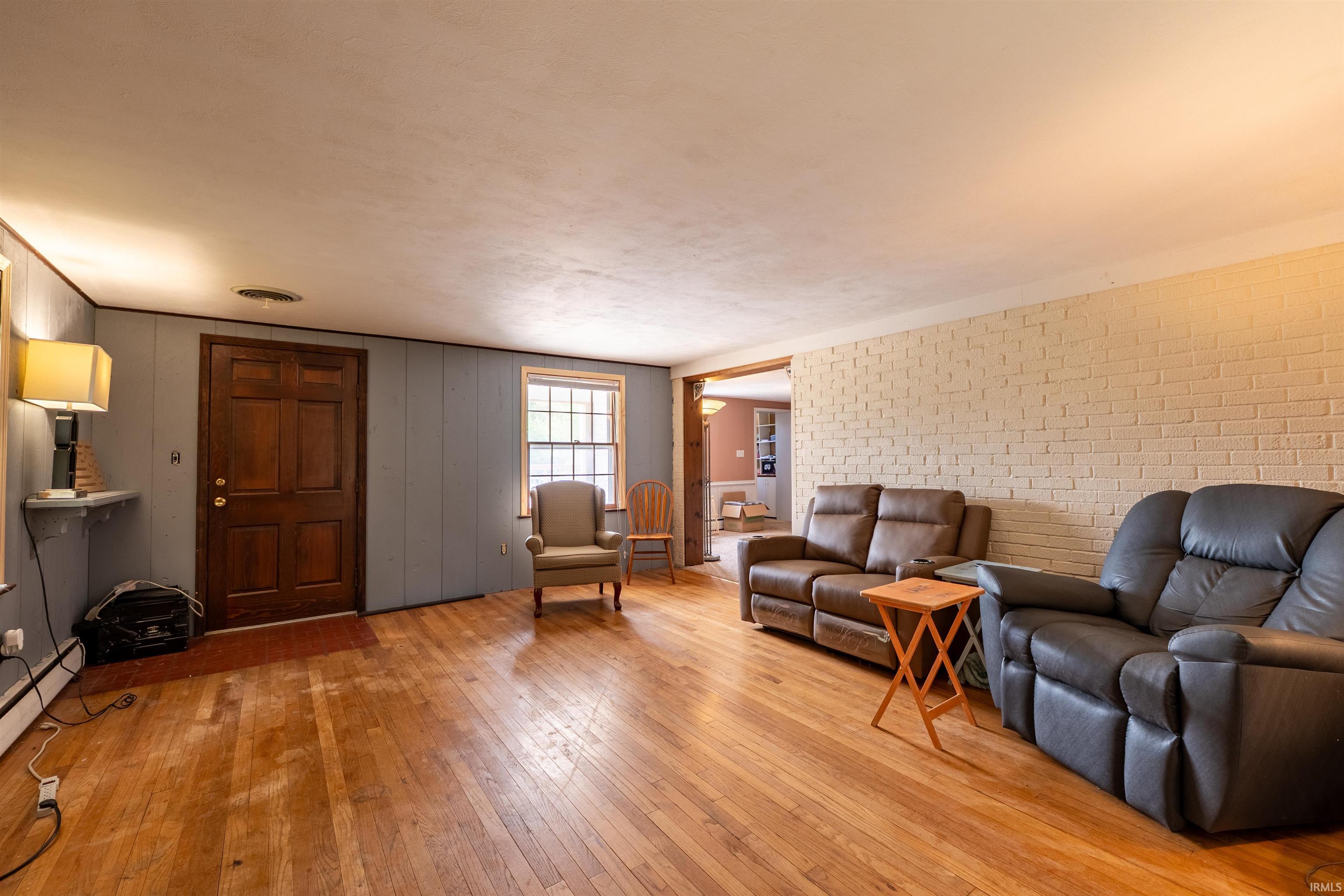 Spacious living area featuring wood-finish flooring, a textured brick accent wall, and light blue vertical wall paneling