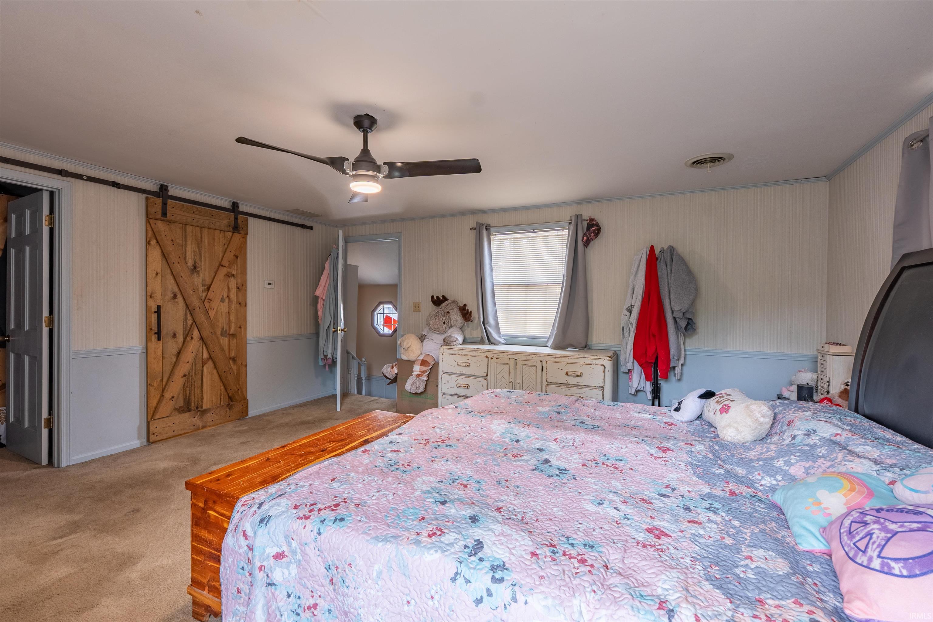 Spacious interior featuring a wood-finish barn door, carpet flooring, a ceiling fan with integrated lighting, and a single window