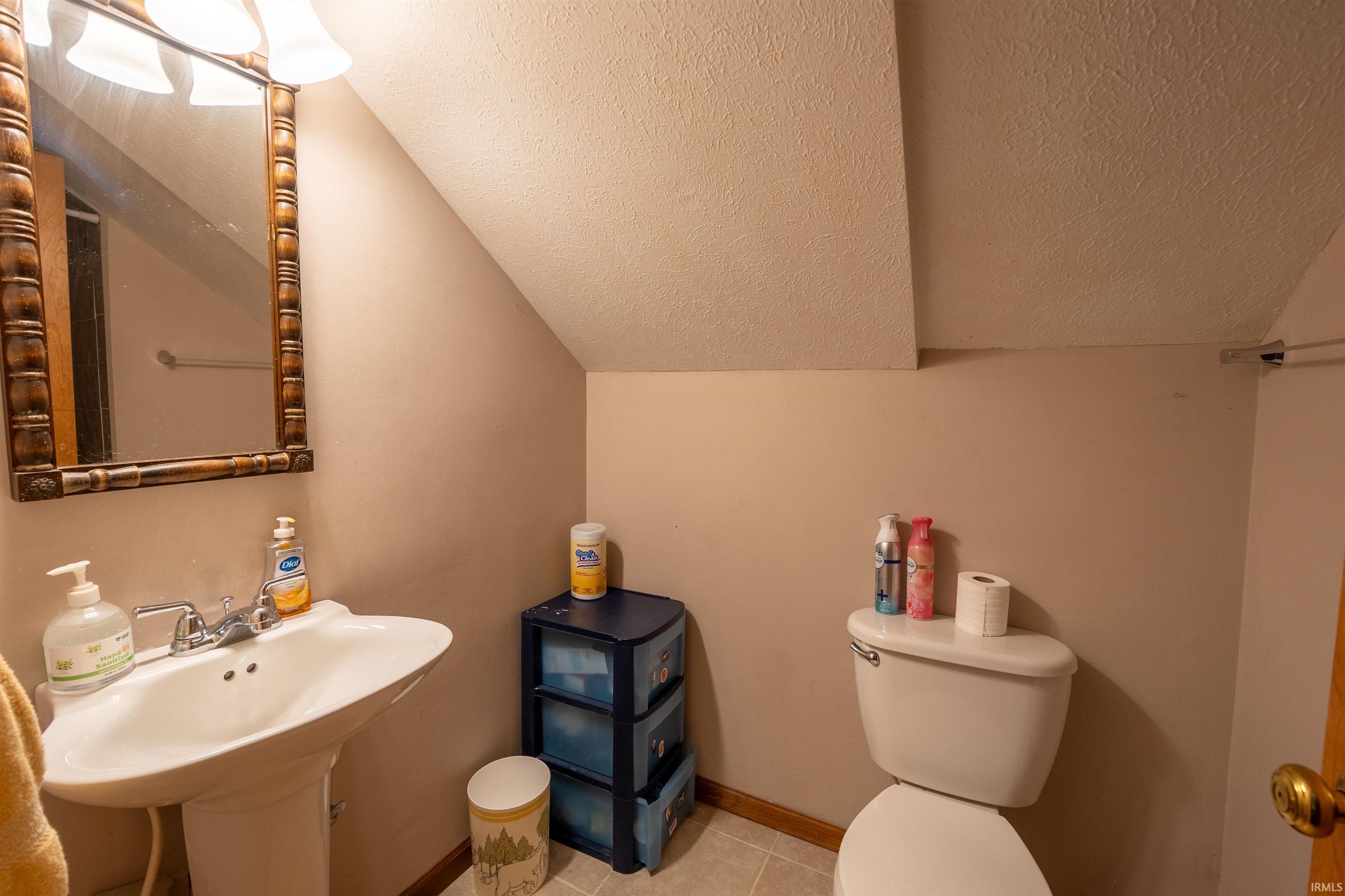 Bathroom featuring a pedestal sink, dual-handle faucet, and an illuminated vanity mirror with a decorative frame