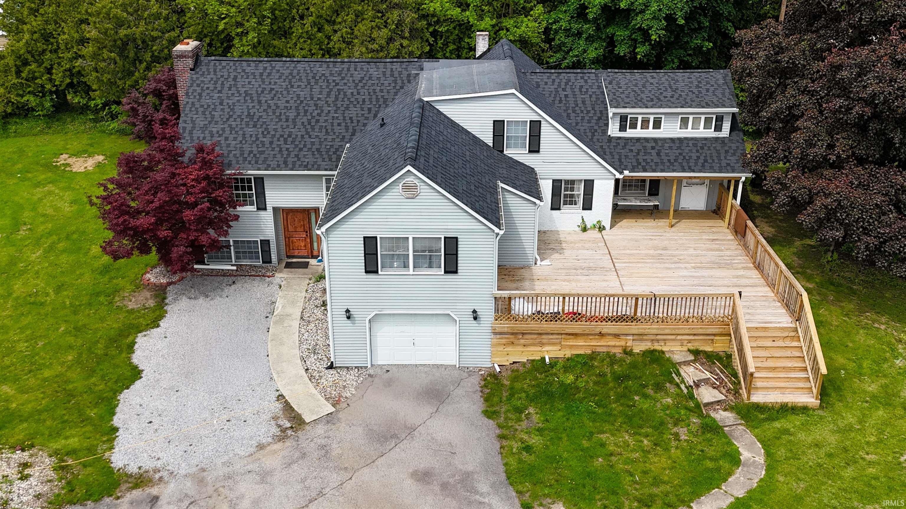 Two-story residence featuring light gray siding with black shutters, a dark shingle roof, and a prominent wood deck