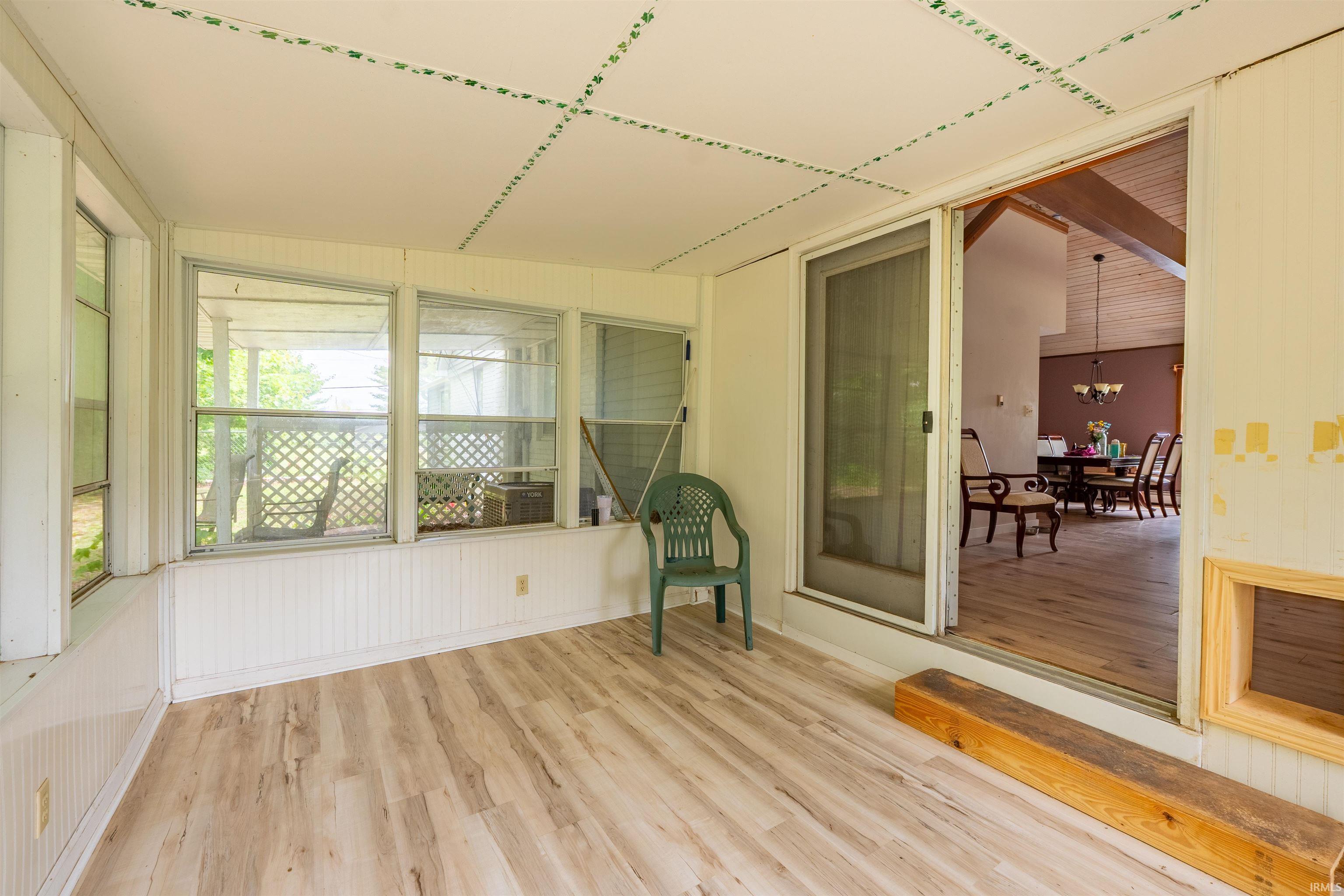 Screened-in porch featuring wood-finish flooring, white beadboard paneling, multiple windows, and a sliding screen door