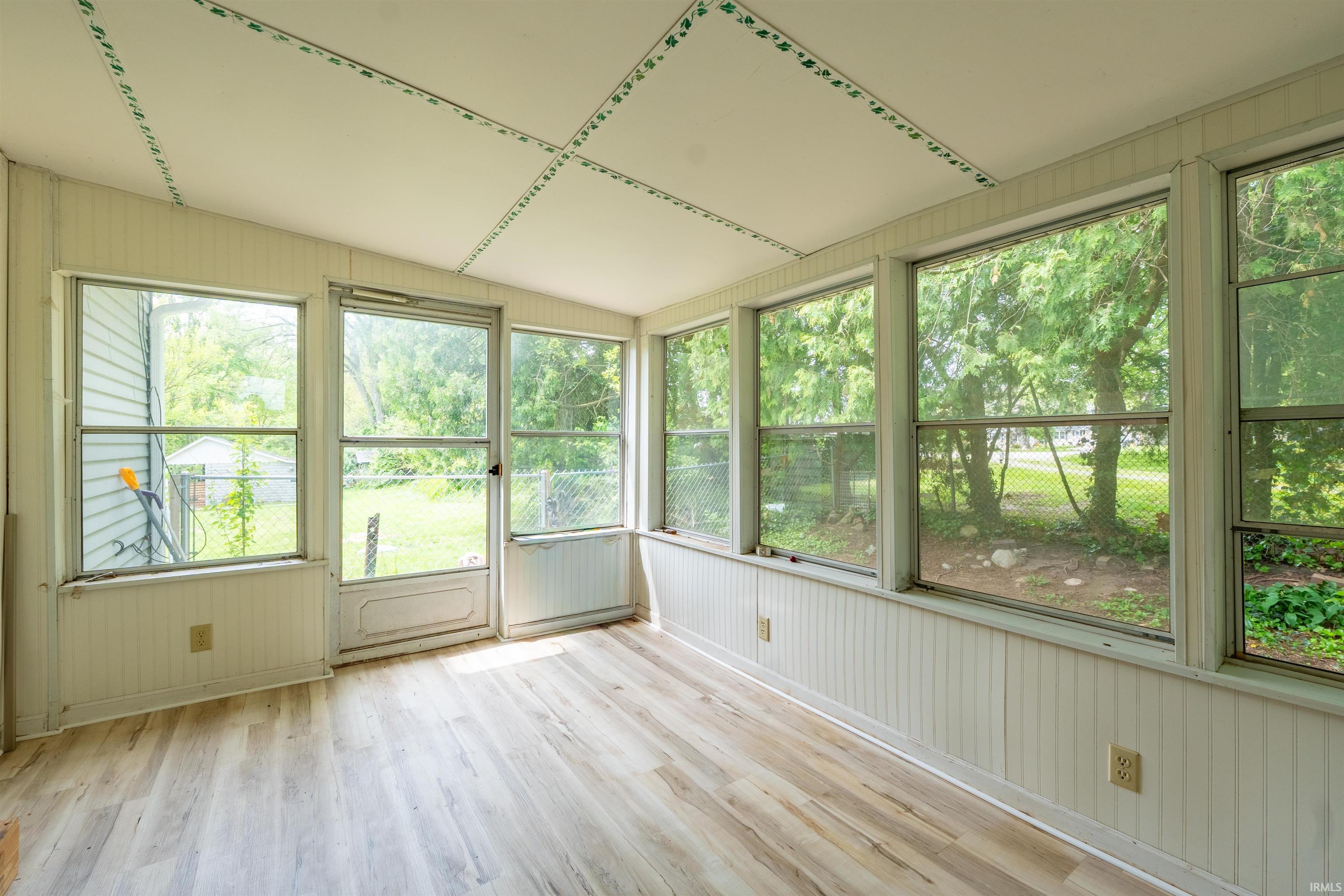 Sunroom featuring extensive window placement, light wood-finish flooring, white beadboard wainscoting, and a full-light door