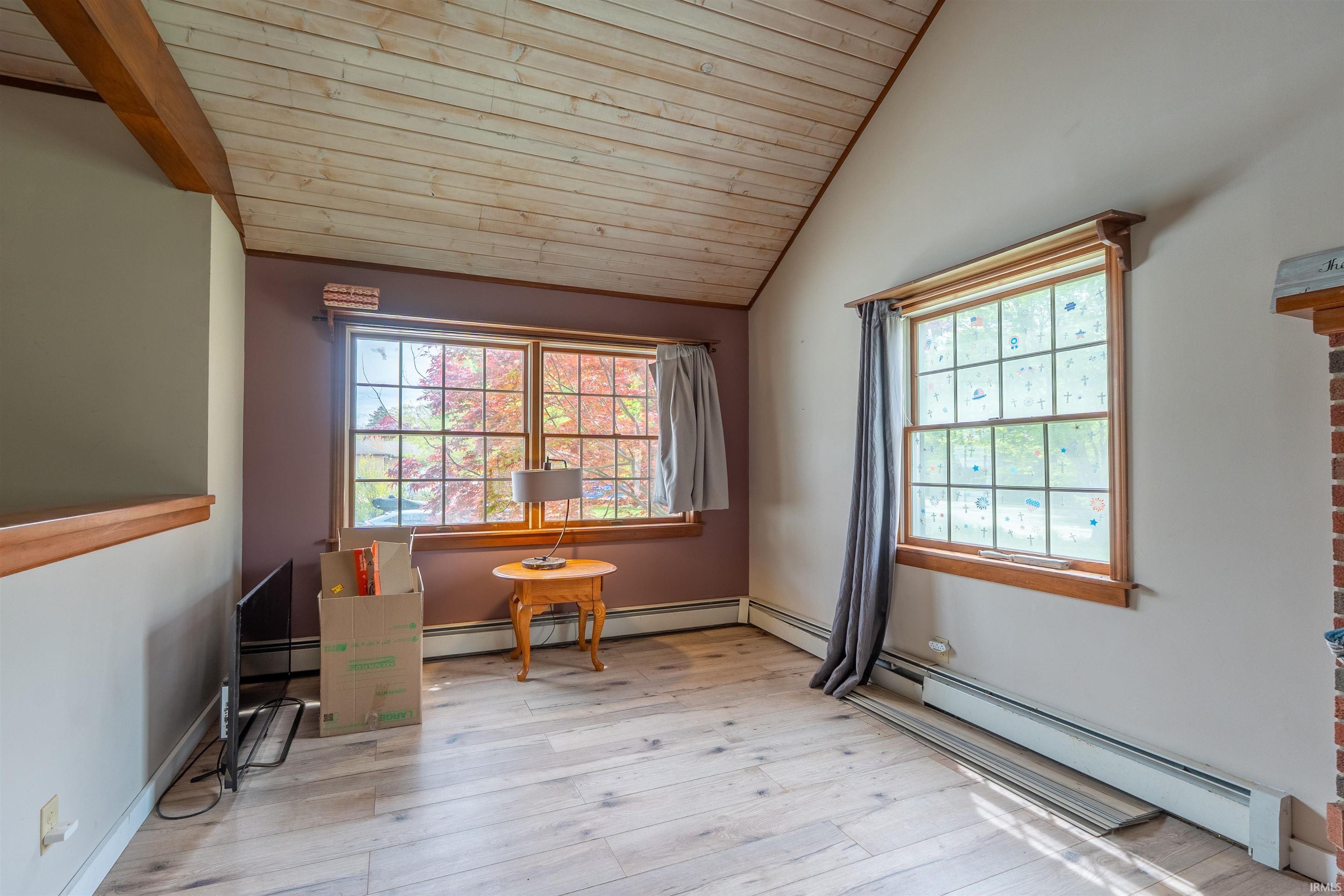 Vaulted wood-finish ceiling with exposed beam, large grid windows with natural wood trim, wood-finish flooring, and baseboard heating