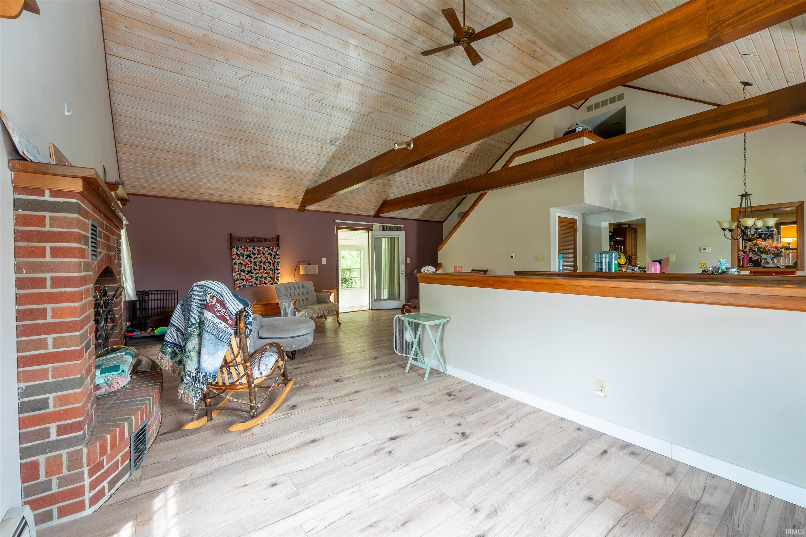 Vaulted wood-planked ceilings with exposed beams, light wood-finish flooring, and a brick fireplace with a wood mantel