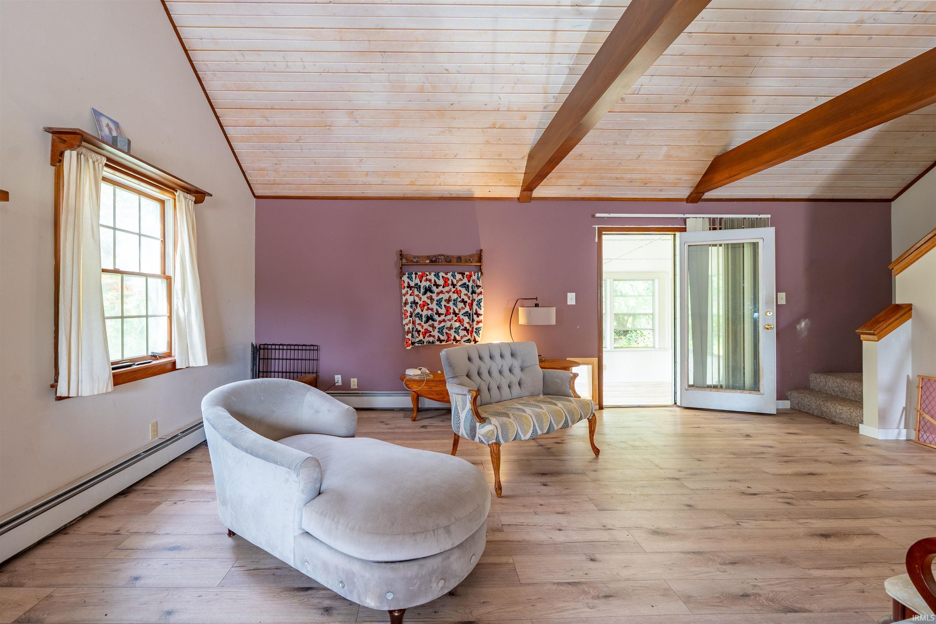 Vaulted wood-finish ceilings with exposed beams, light wood-finish flooring, and a glass-paneled exterior door