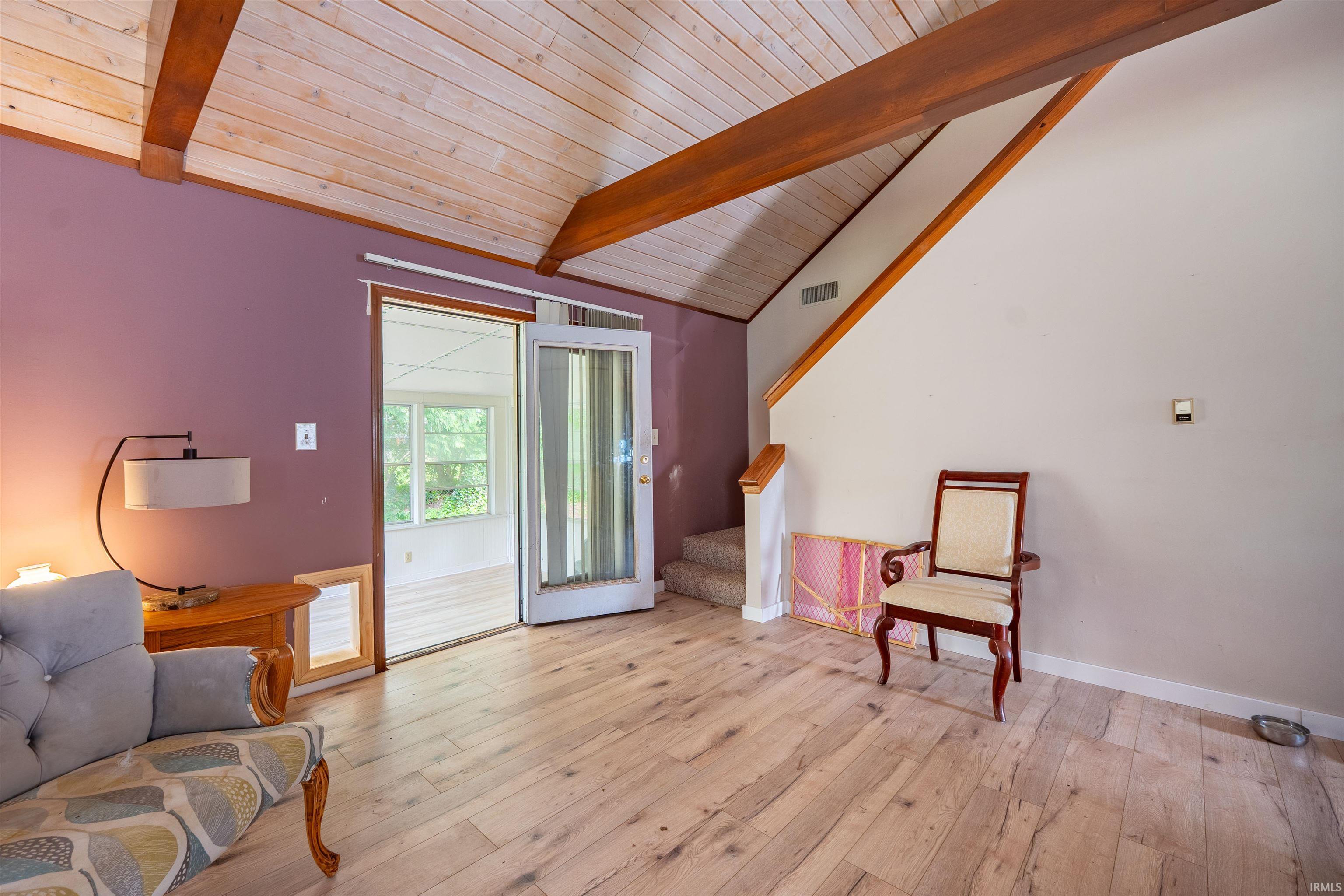Vaulted wood-plank ceiling with exposed wood beams, light wood-finish flooring, and a glass-paneled patio door opening to an enclosed porch