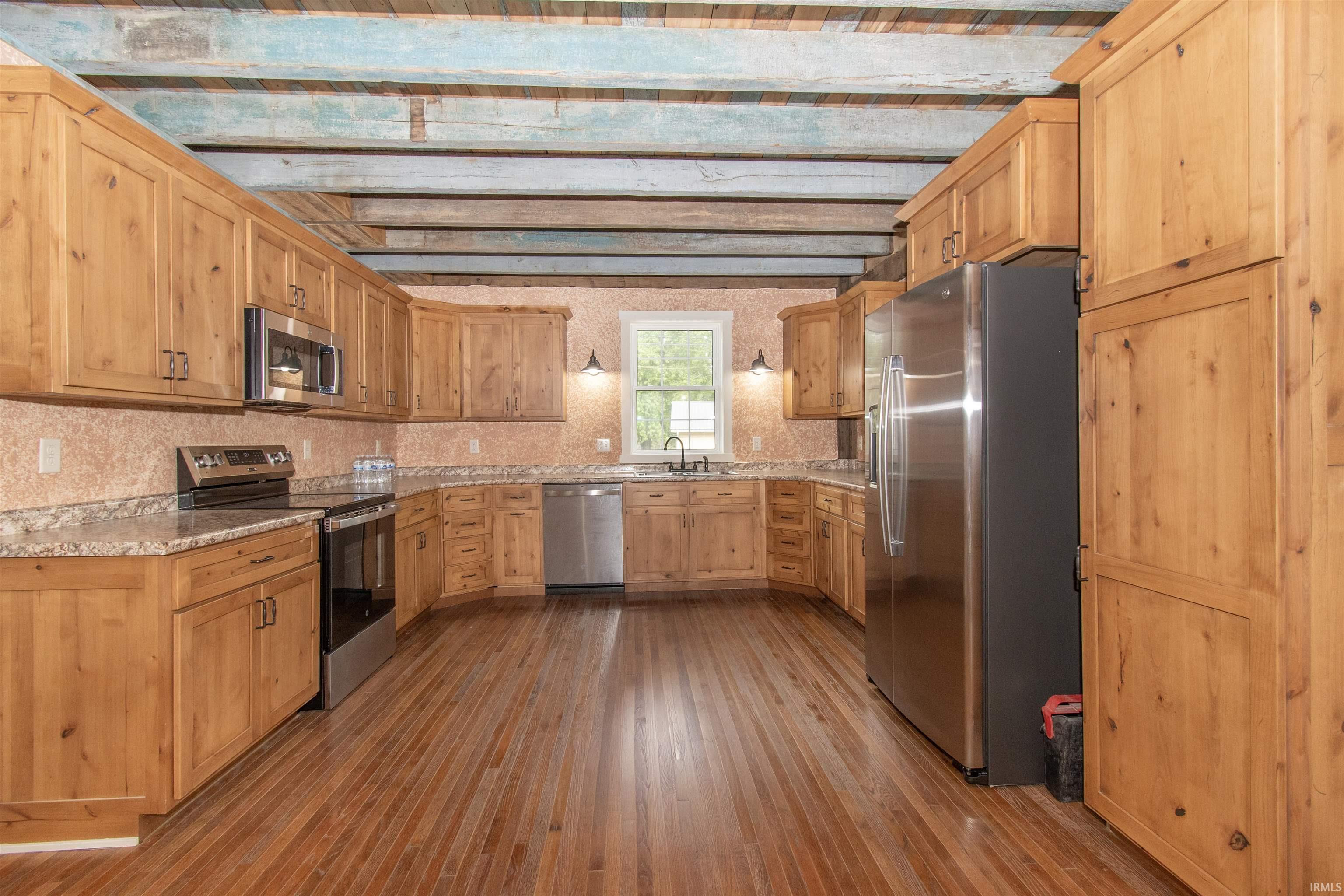 Spacious kitchen featuring extensive light wood cabinetry, wood-finish flooring, light-toned countertops, and stainless steel appliances