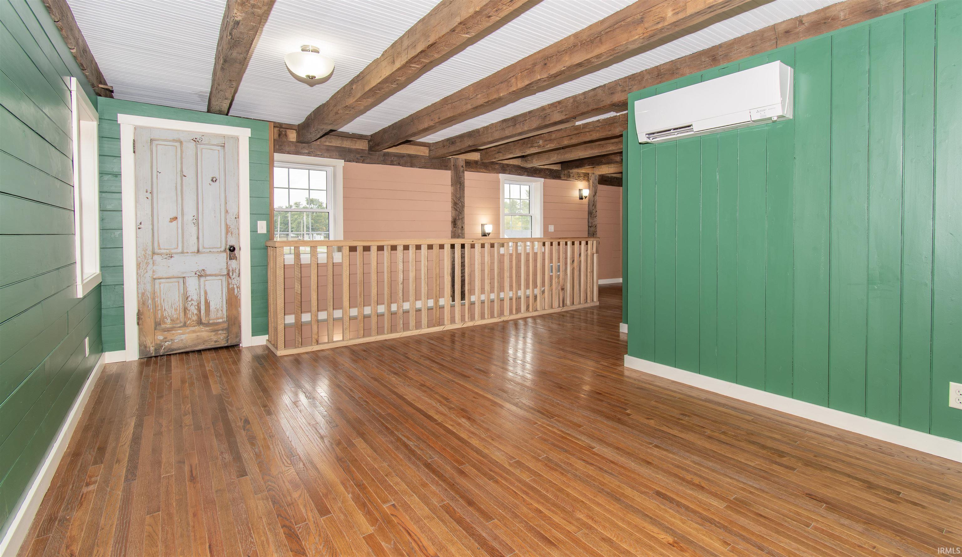 Hardwood flooring throughout, exposed wood ceiling beams, white beadboard ceiling, a distressed wooden door, and a mini-split system