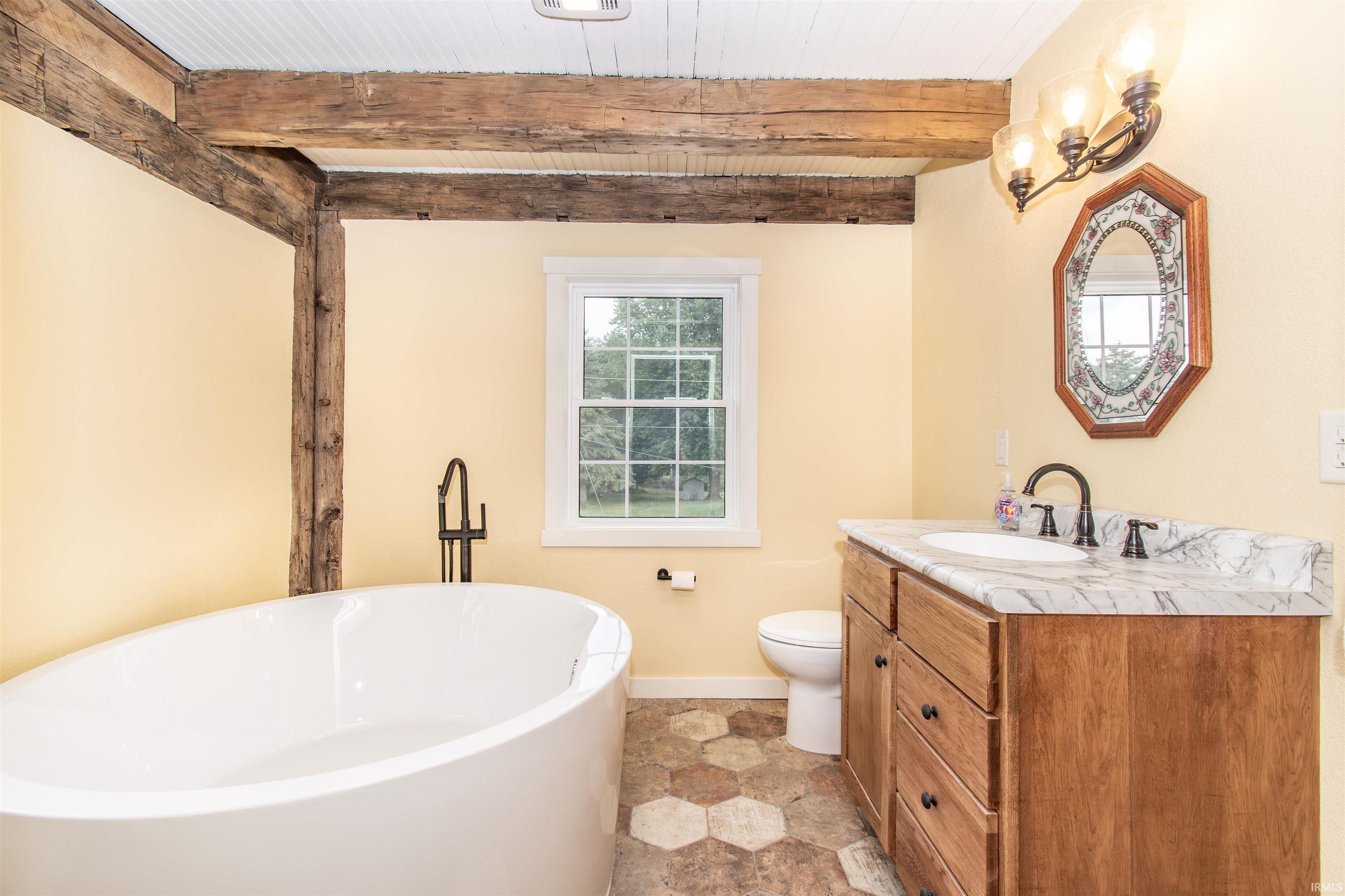 Freestanding soaking tub with a floor-mounted fixture, complemented by a wood vanity with a stone countertop and under-mount sink