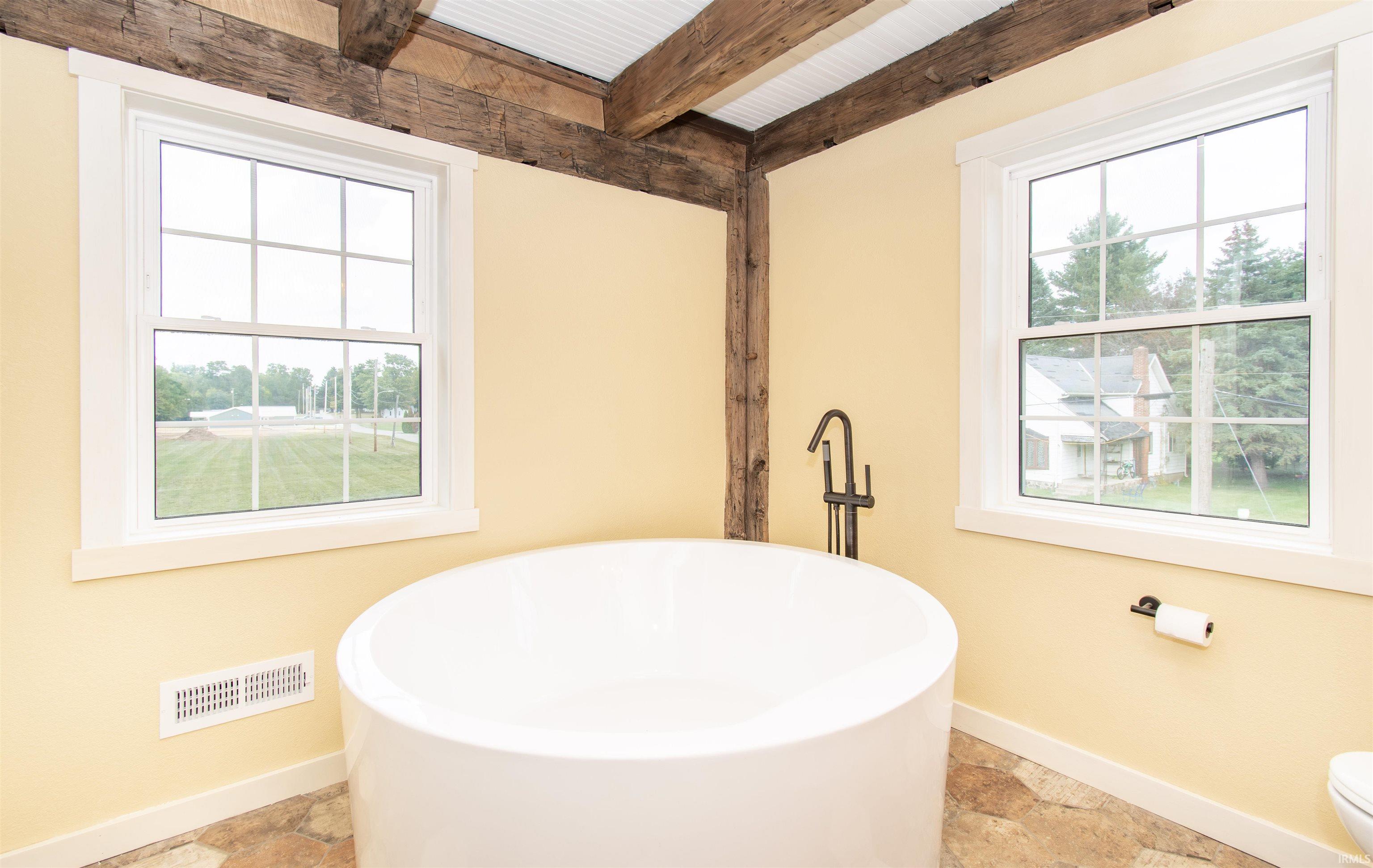 Freestanding circular soaking tub with a floor-mounted dark bronze faucet set, exposed rustic wood ceiling beams, and paneled ceilings