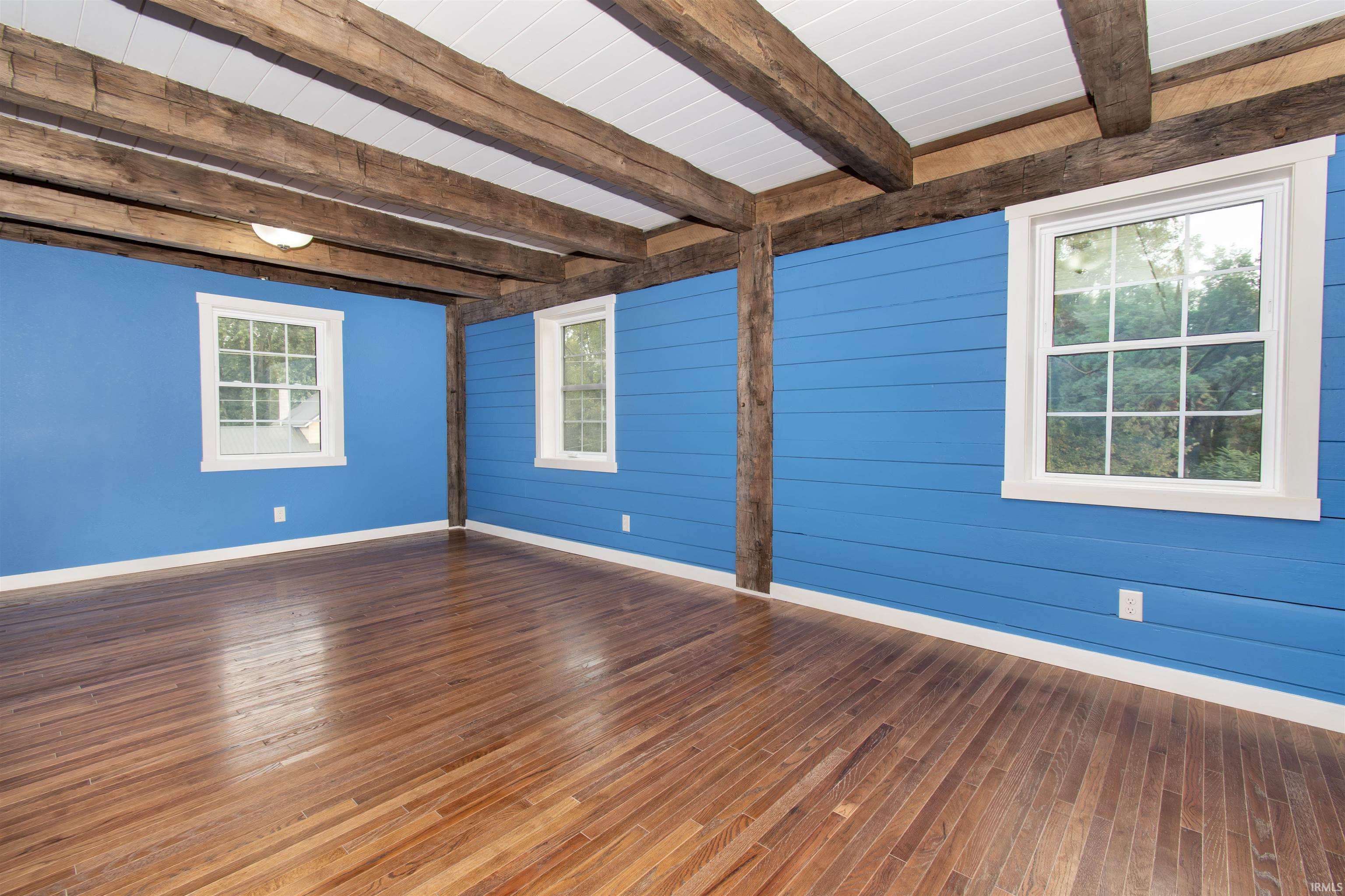 Exposed wood beams accentuating the ceiling, wood-finish flooring, and two double-hung windows with white trim