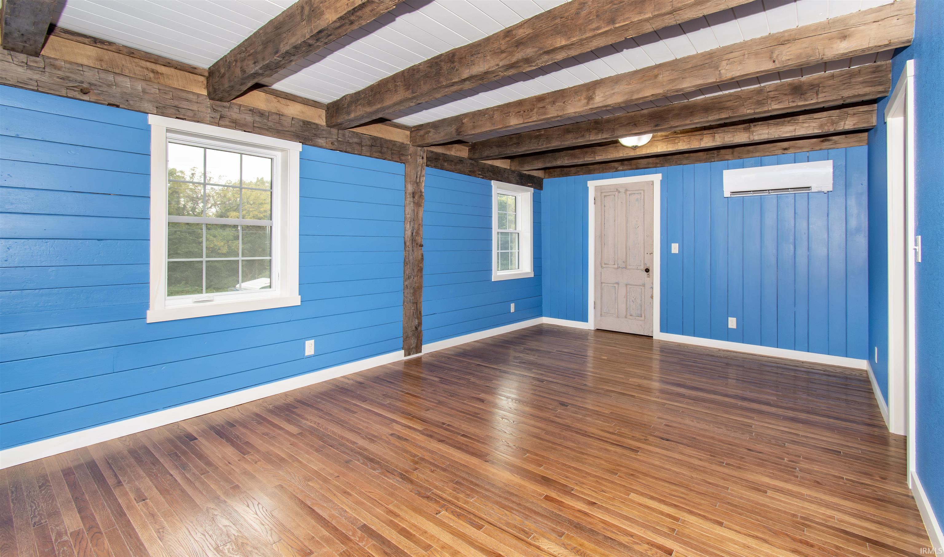 Hardwood flooring throughout featuring exposed wood ceiling beams, white trim, and blue paneled walls