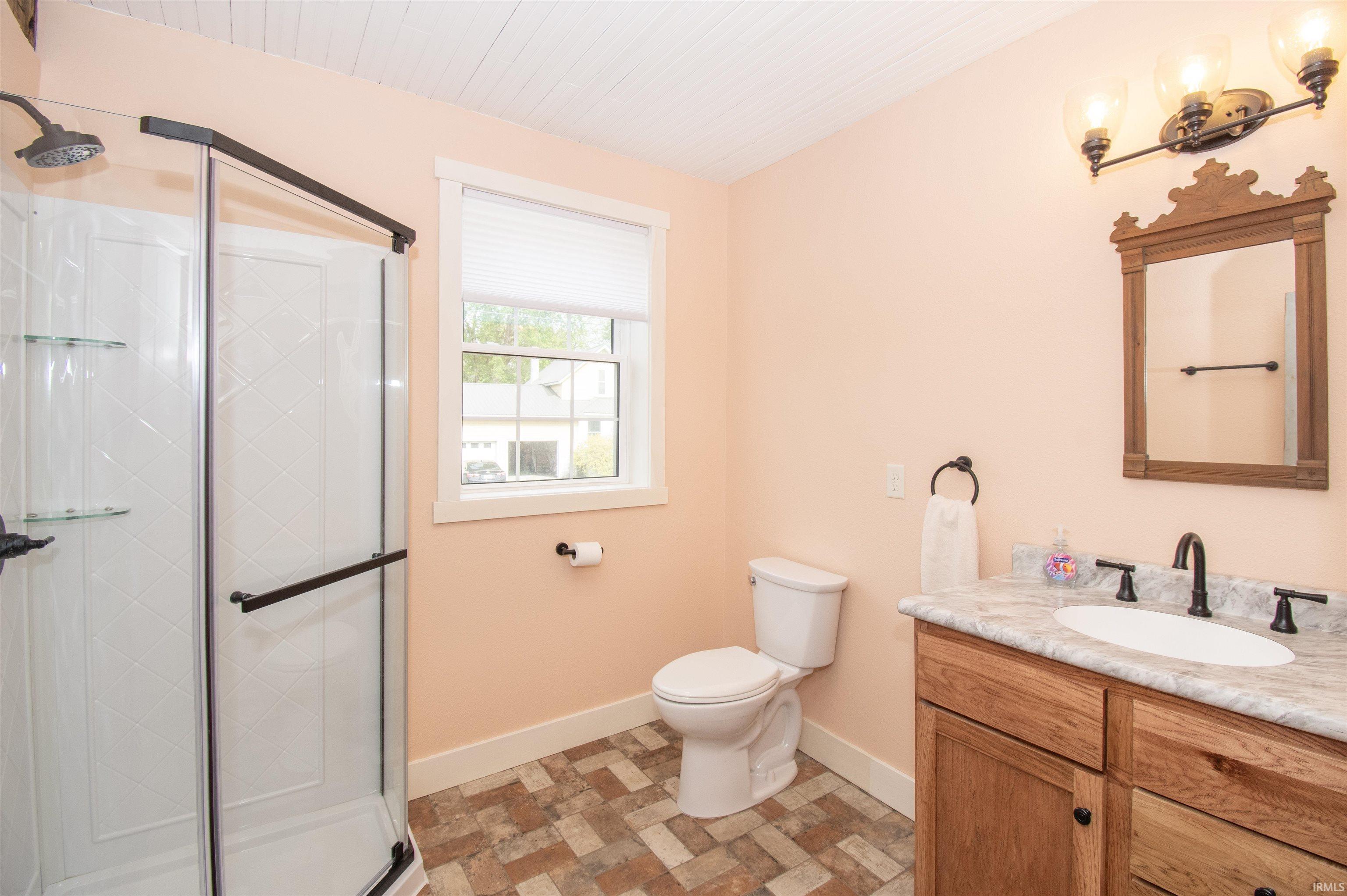 Bathroom featuring a corner shower with glass enclosure and dark hardware, wood-finish vanity with an undermount sink, countertop, and dark faucet, a wood-framed mirror, and patterned floor tile