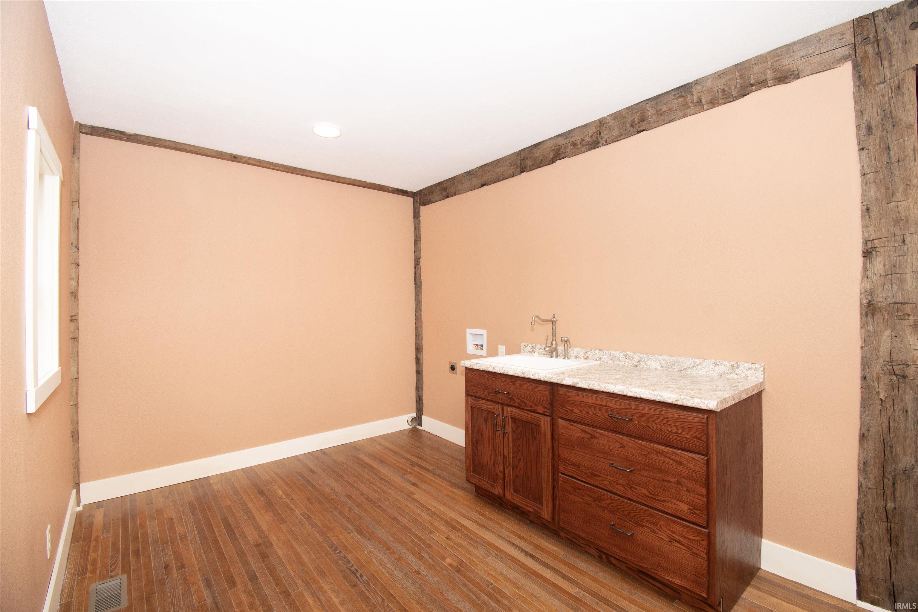 Room featuring exposed wood beams, hardwood flooring, and a built-in vanity with a sink and stone countertop