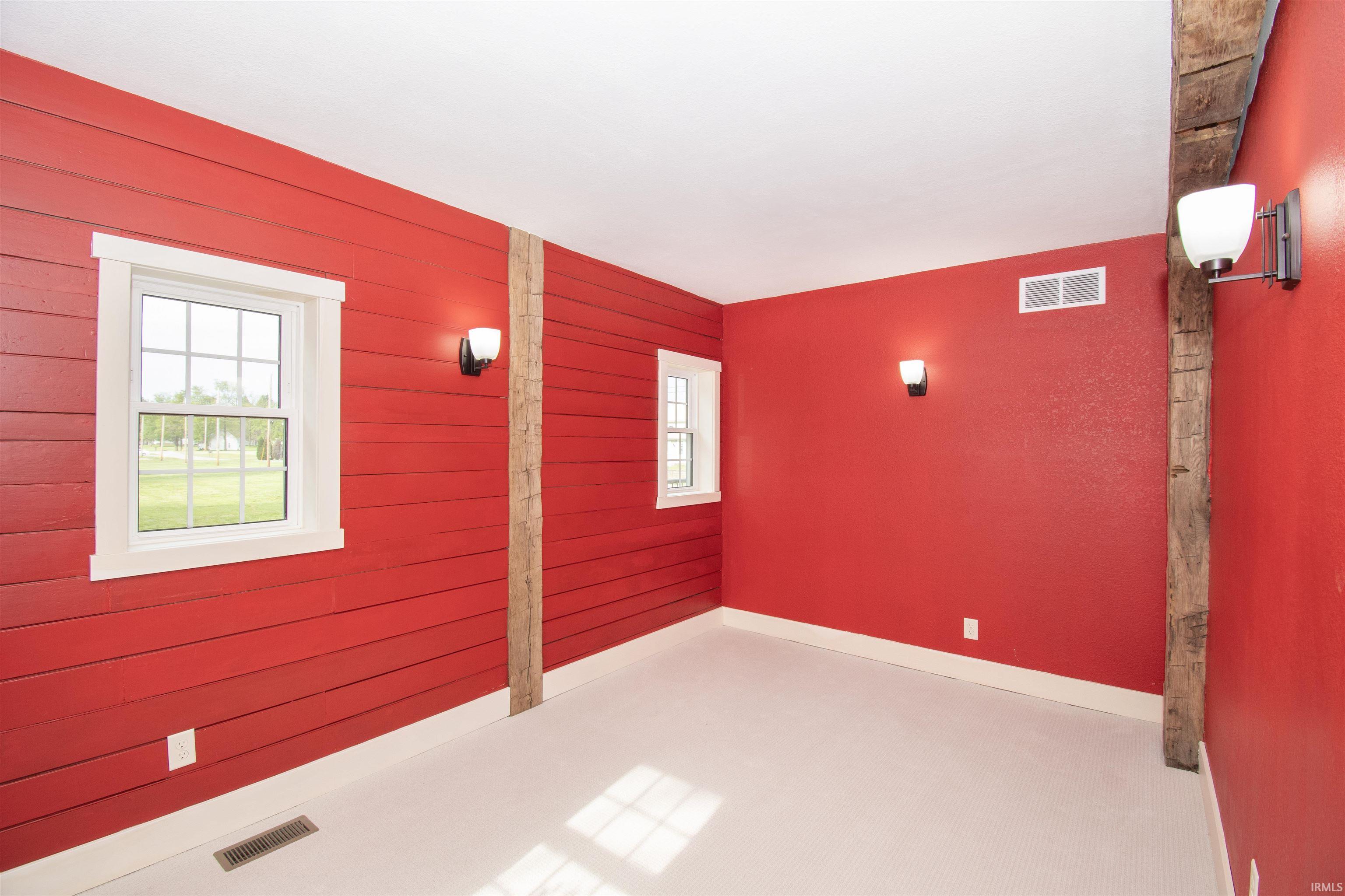Interior space featuring red horizontal wall paneling, white trim, two grid-pattern windows, exposed timber beam, and wall-mounted light fixtures