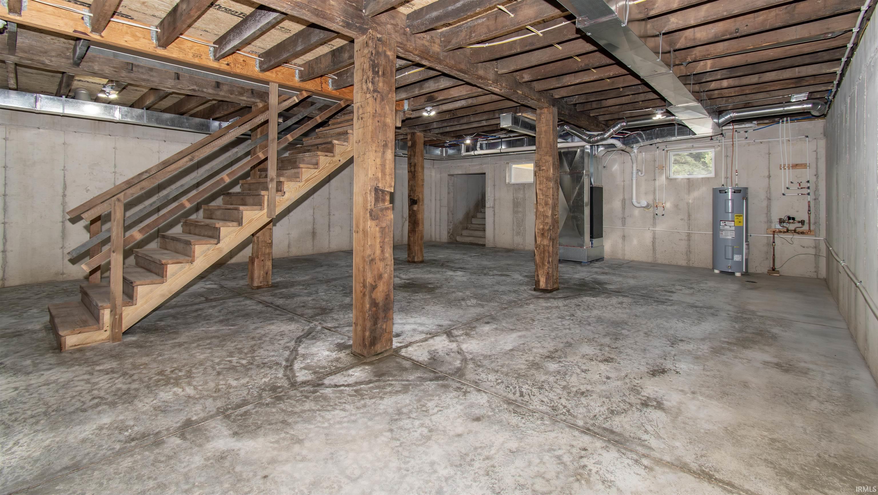 Spacious unfinished basement featuring a concrete floor, exposed wood ceiling joists, and sturdy structural columns