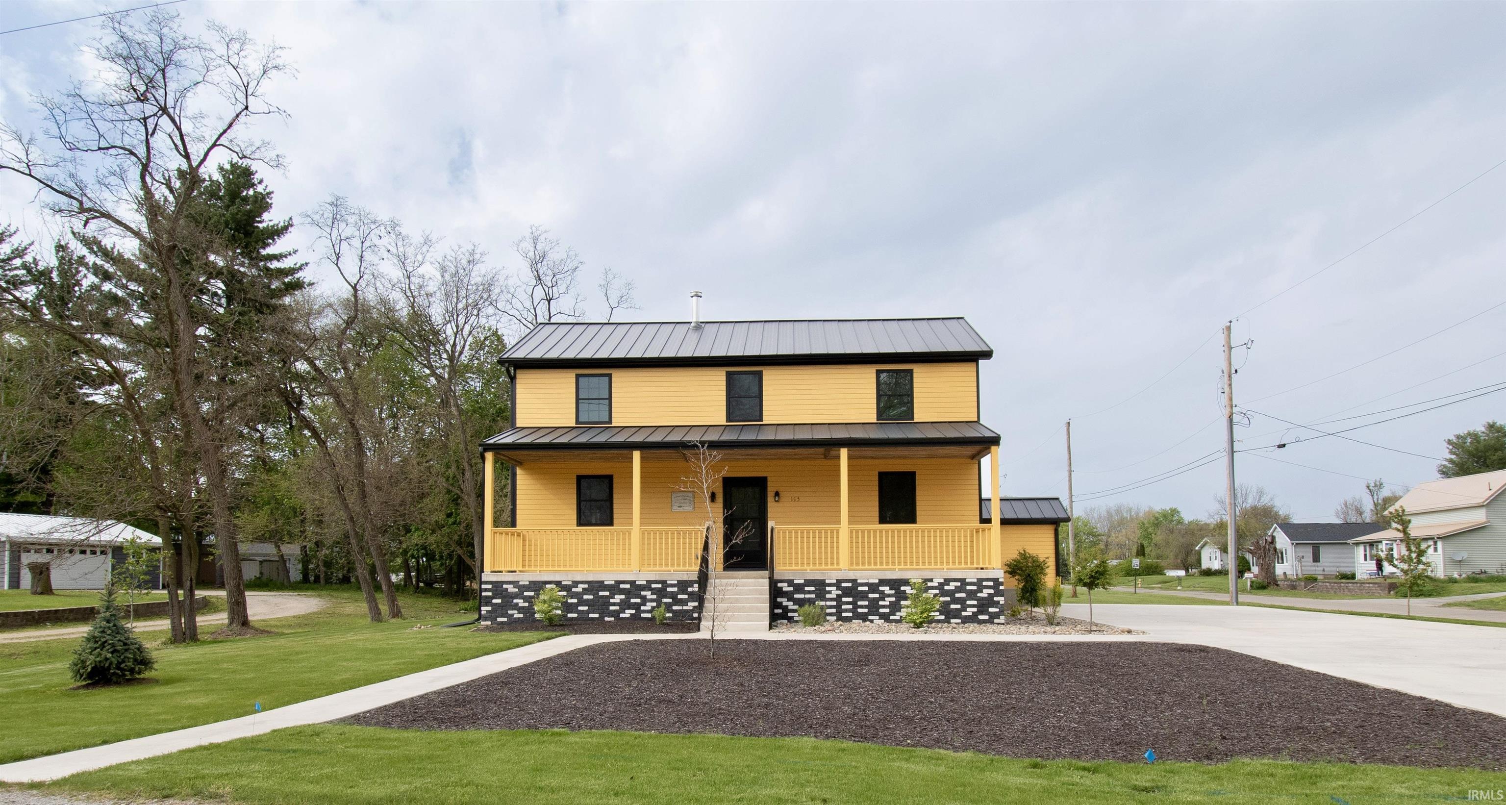 Two-story residence featuring a bold yellow exterior, dark metal roof, and a covered front porch with railing