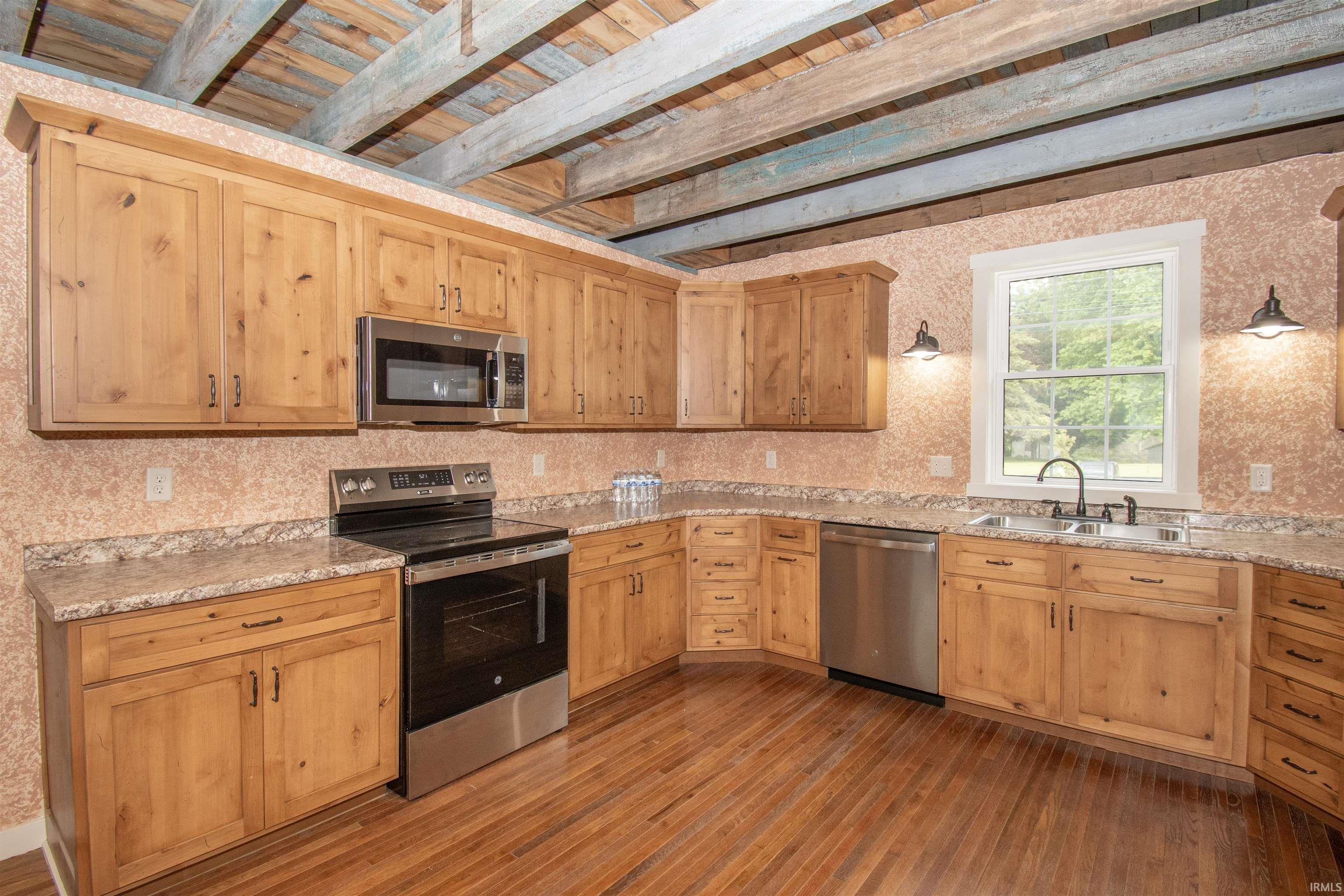 Kitchen featuring wood-finish flooring, natural wood cabinetry, light-toned countertops, stainless steel appliances, and exposed ceiling beams