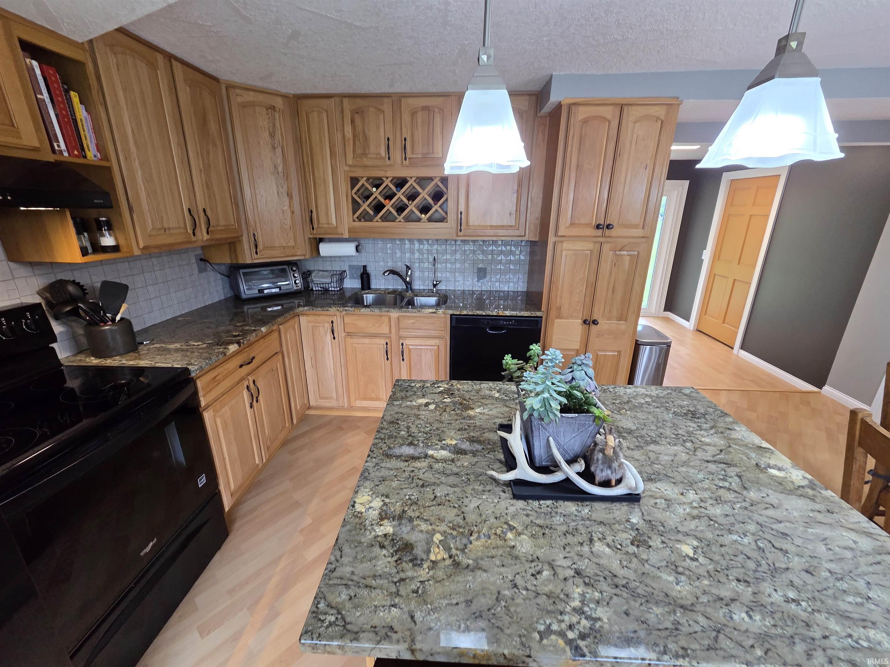 Kitchen featuring light wood cabinetry, granite countertops, a tile backsplash, and wood-finish flooring